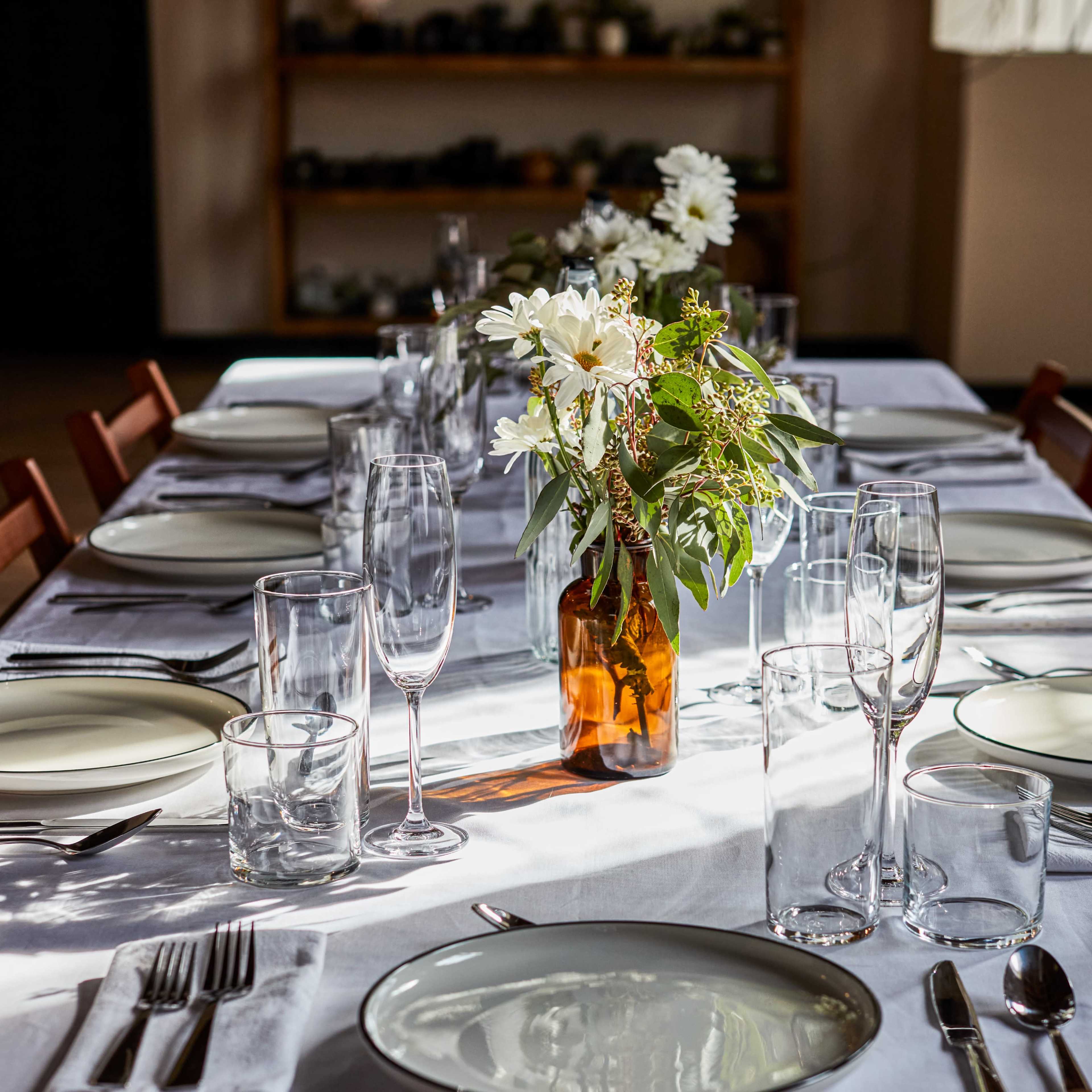 A elegantly set dining table with plates, glassware, and a vase of flowers as the centerpiece.