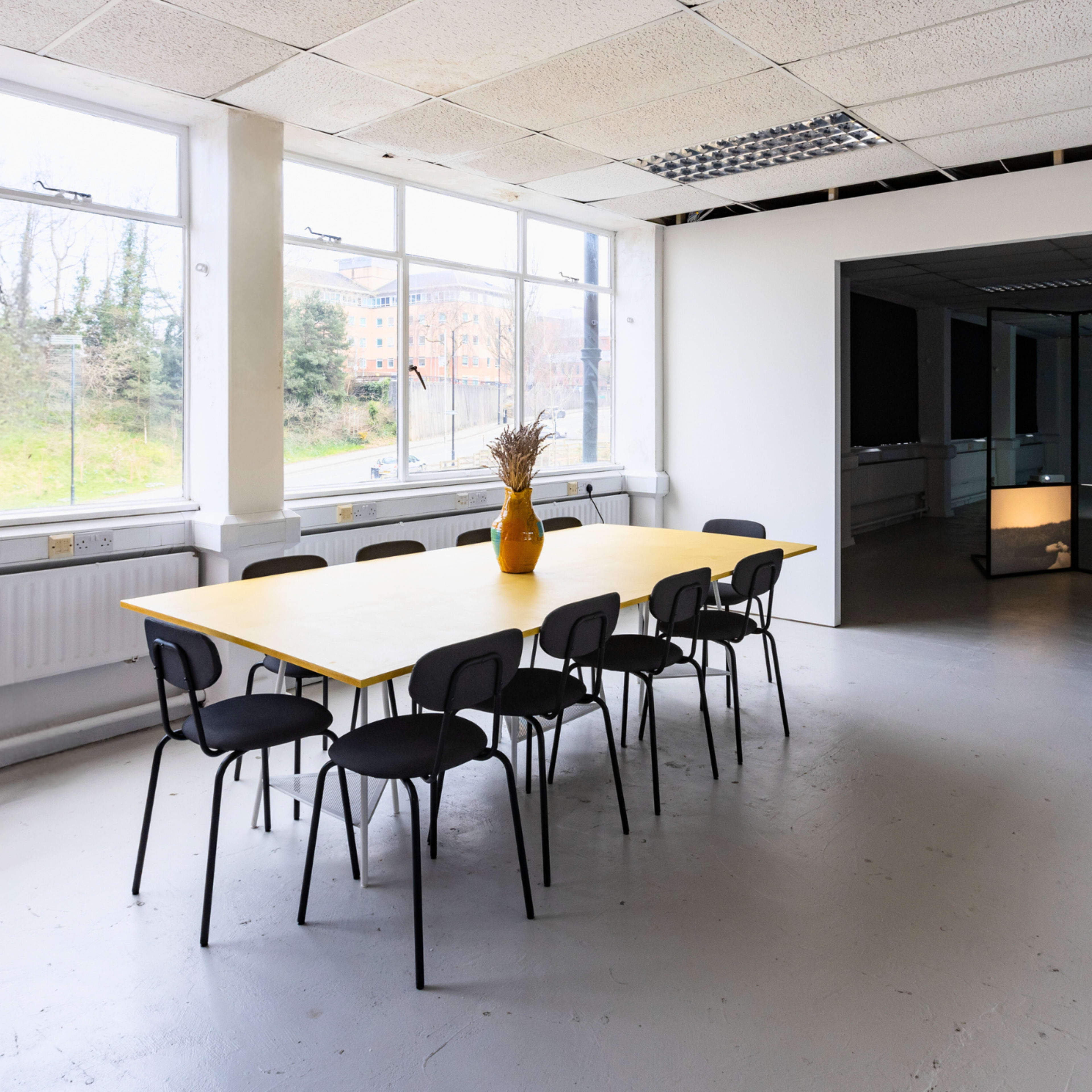 A spacious office interior with a large yellow table surrounded by black chairs and a view of a hallway leading to another room.