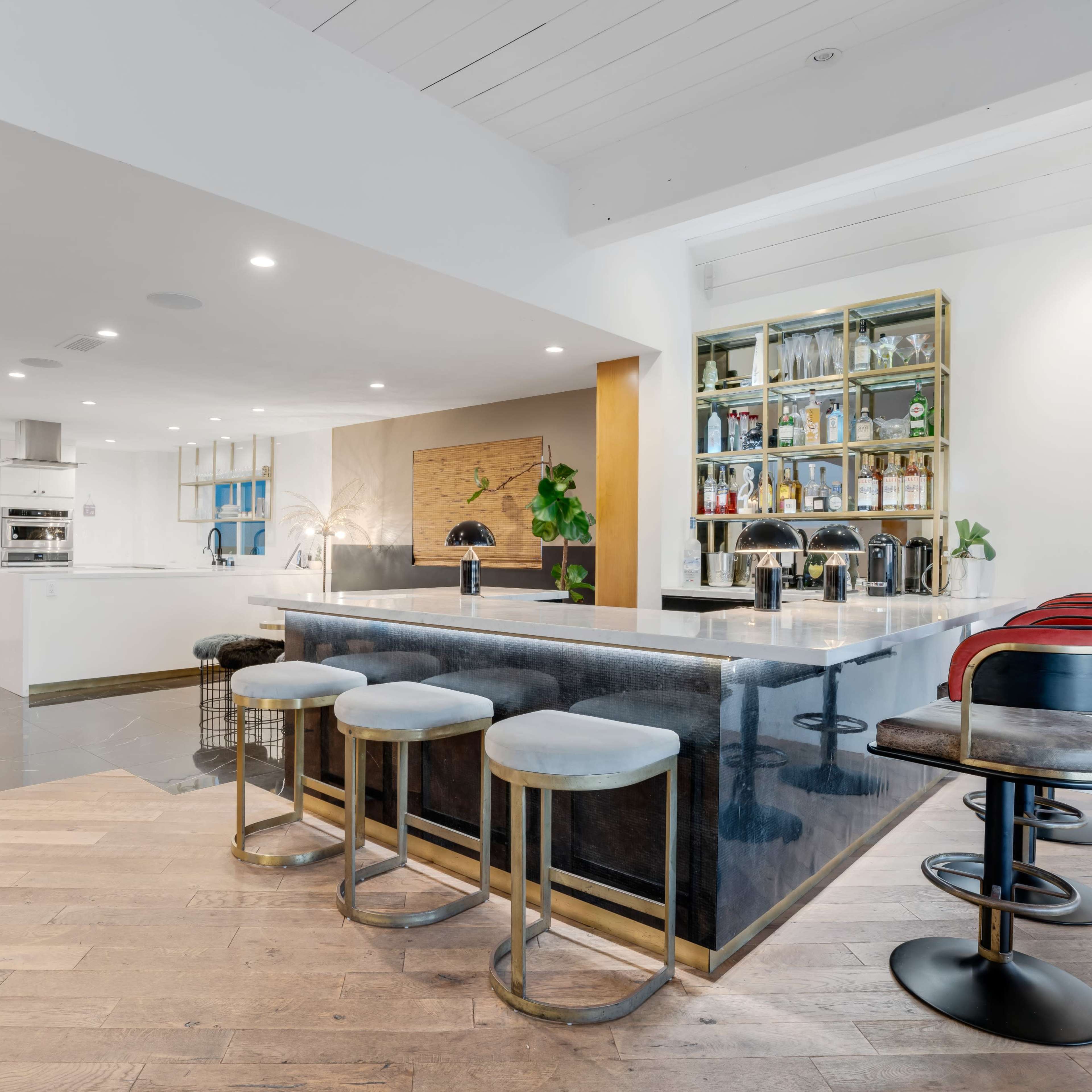 A modern kitchen with a large island bar featuring stools, glass shelves displaying bottles, and a spacious layout.