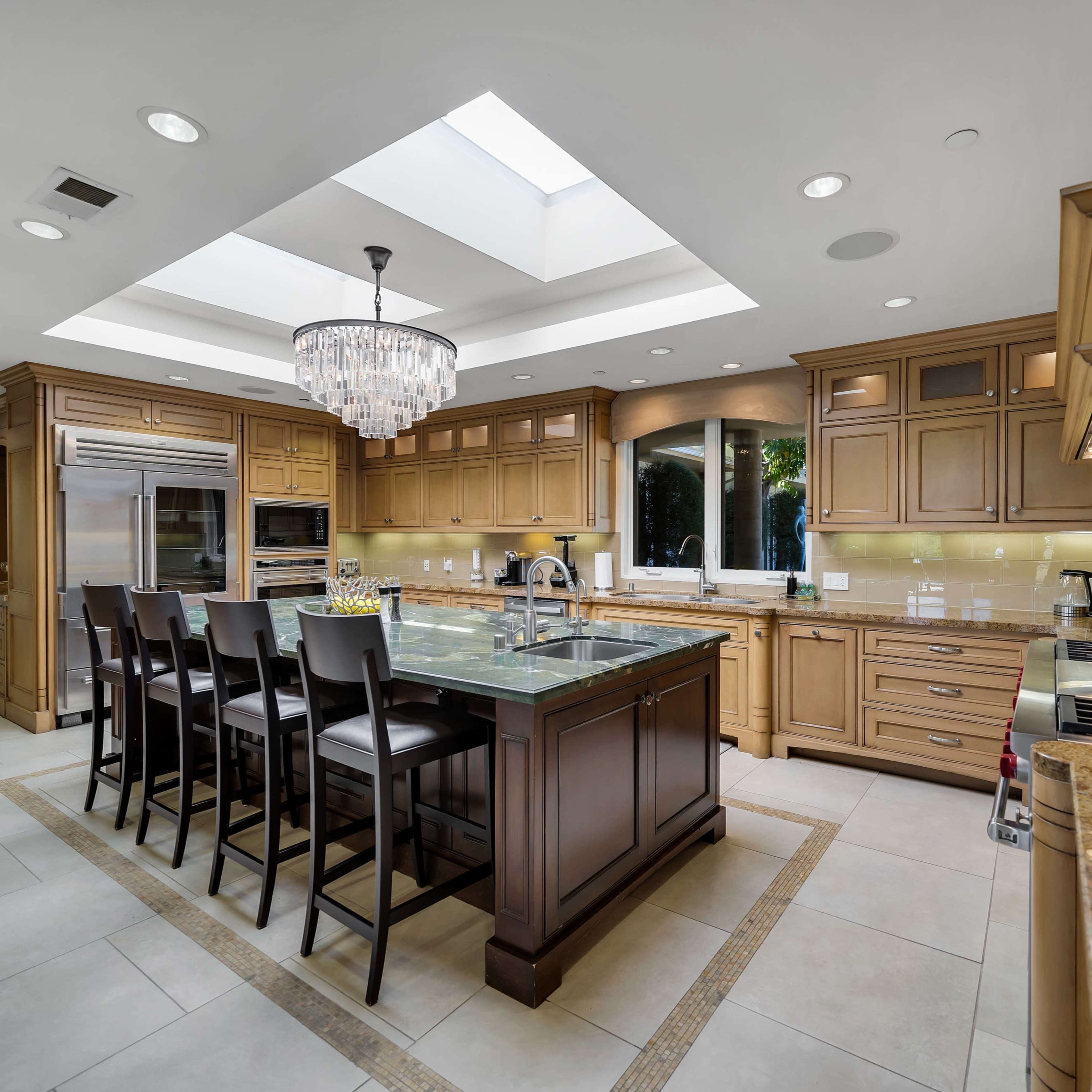 A spacious kitchen features a central island with seating, wooden cabinetry, and a skylight that illuminates the area.
