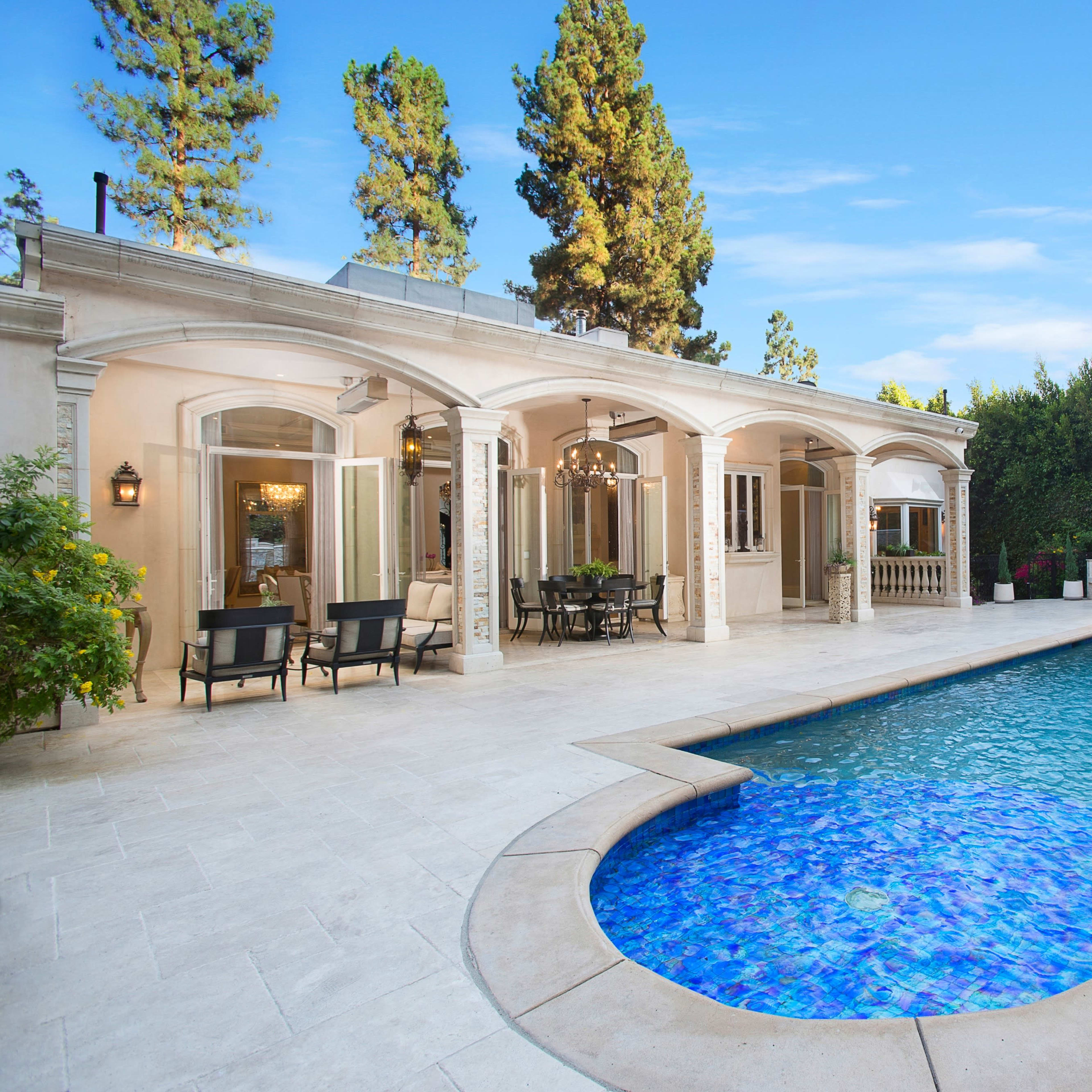 A luxurious outdoor area featuring a swimming pool with a waterfall, surrounded by a stone-paved patio and elegant seating arrangements.