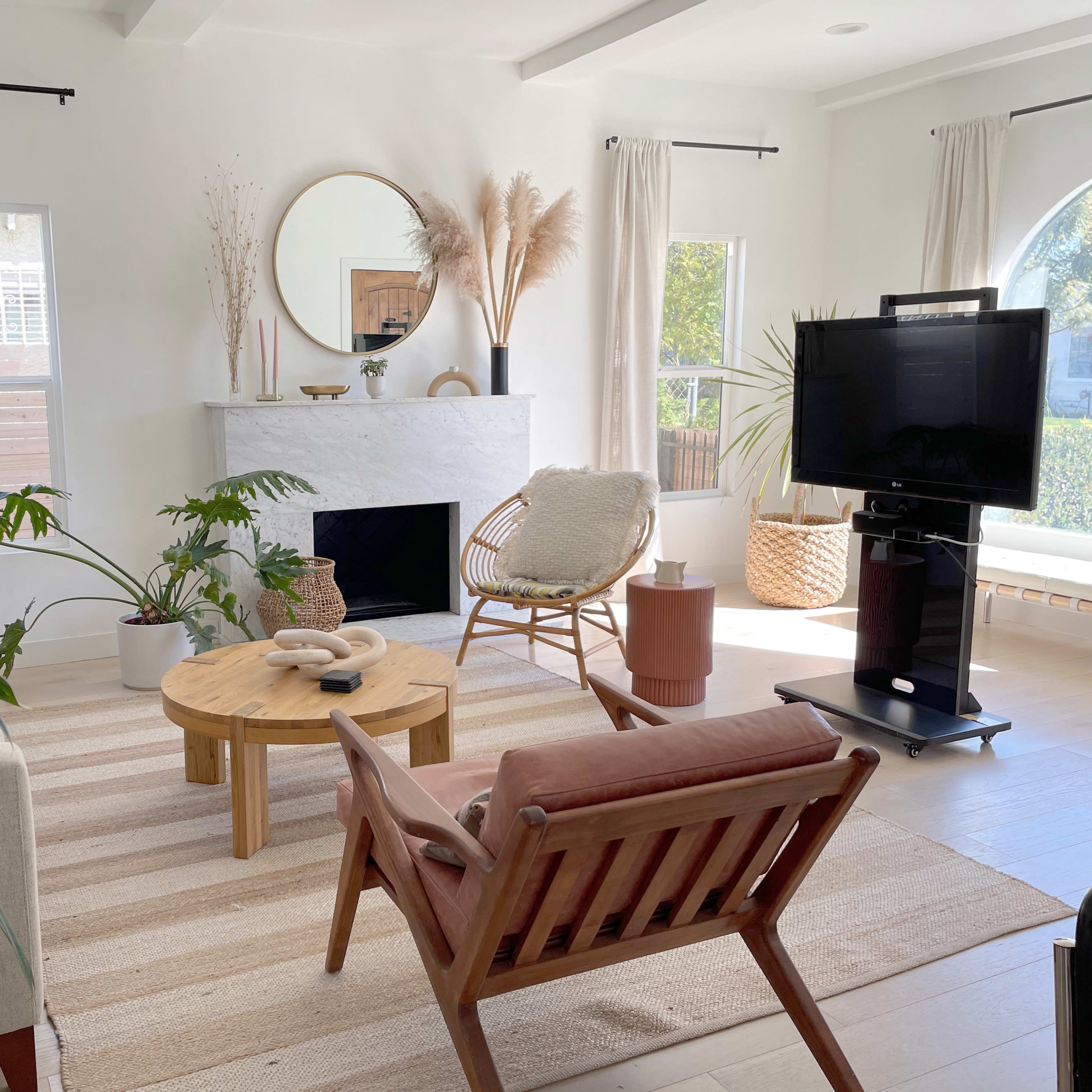 A bright, modern living room featuring a circular mirror above a white fireplace, a round wooden coffee table, a plant, and various seating options.