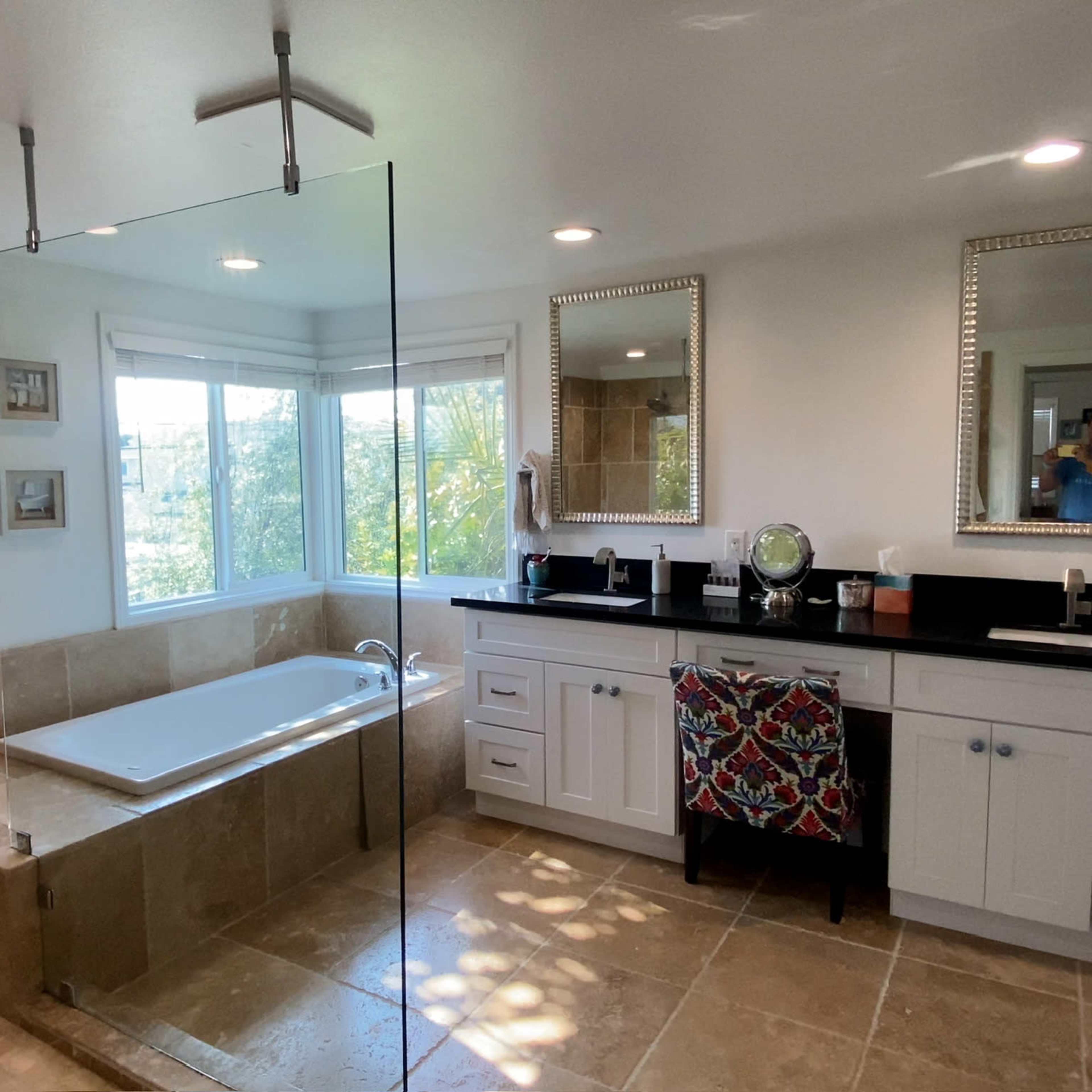 A spacious bathroom features a glass-enclosed shower, a freestanding bathtub, a double vanity with mirrors, and a large window providing natural light.