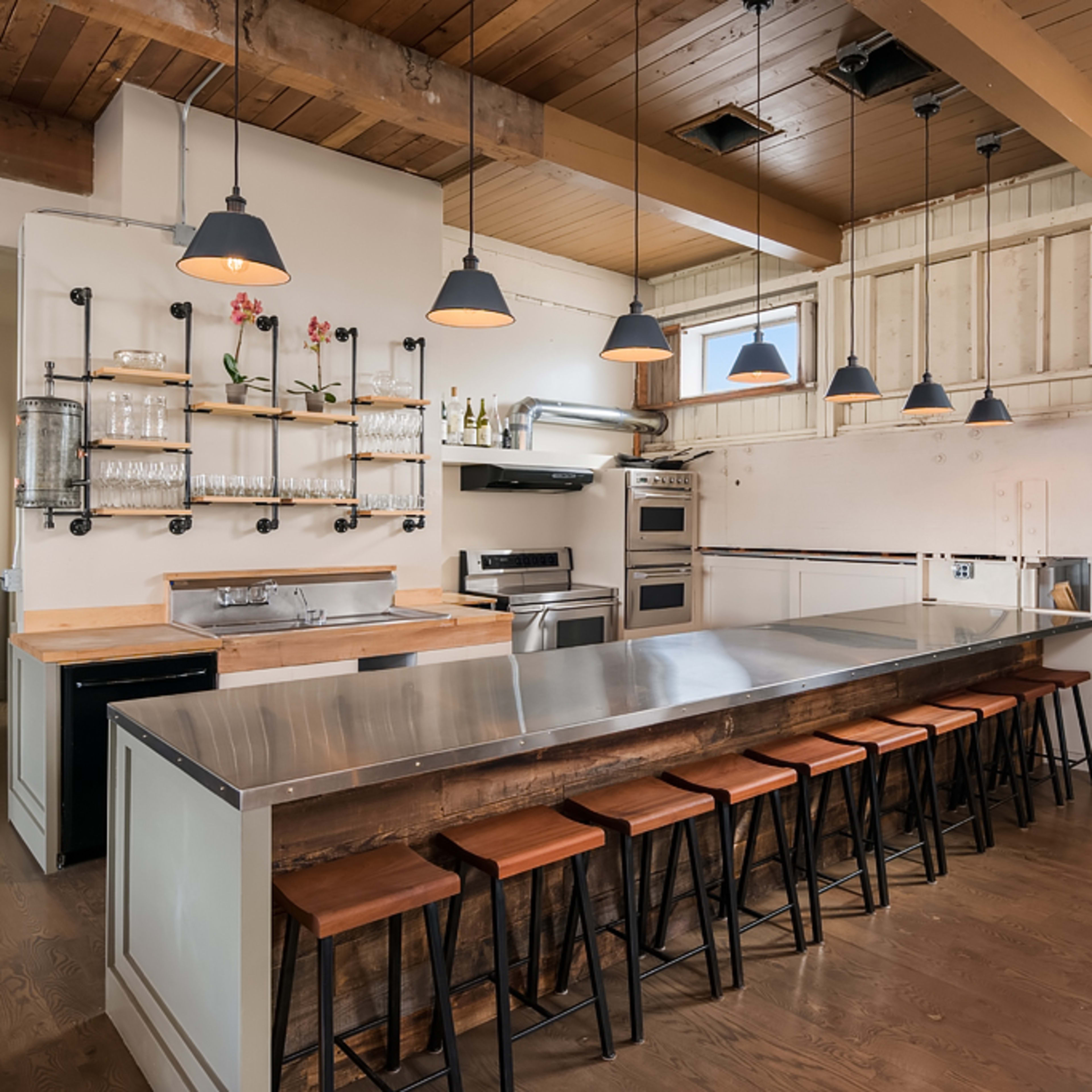 A modern kitchen with a stainless steel countertop, several hanging pendant lights, and a row of wooden bar stools.