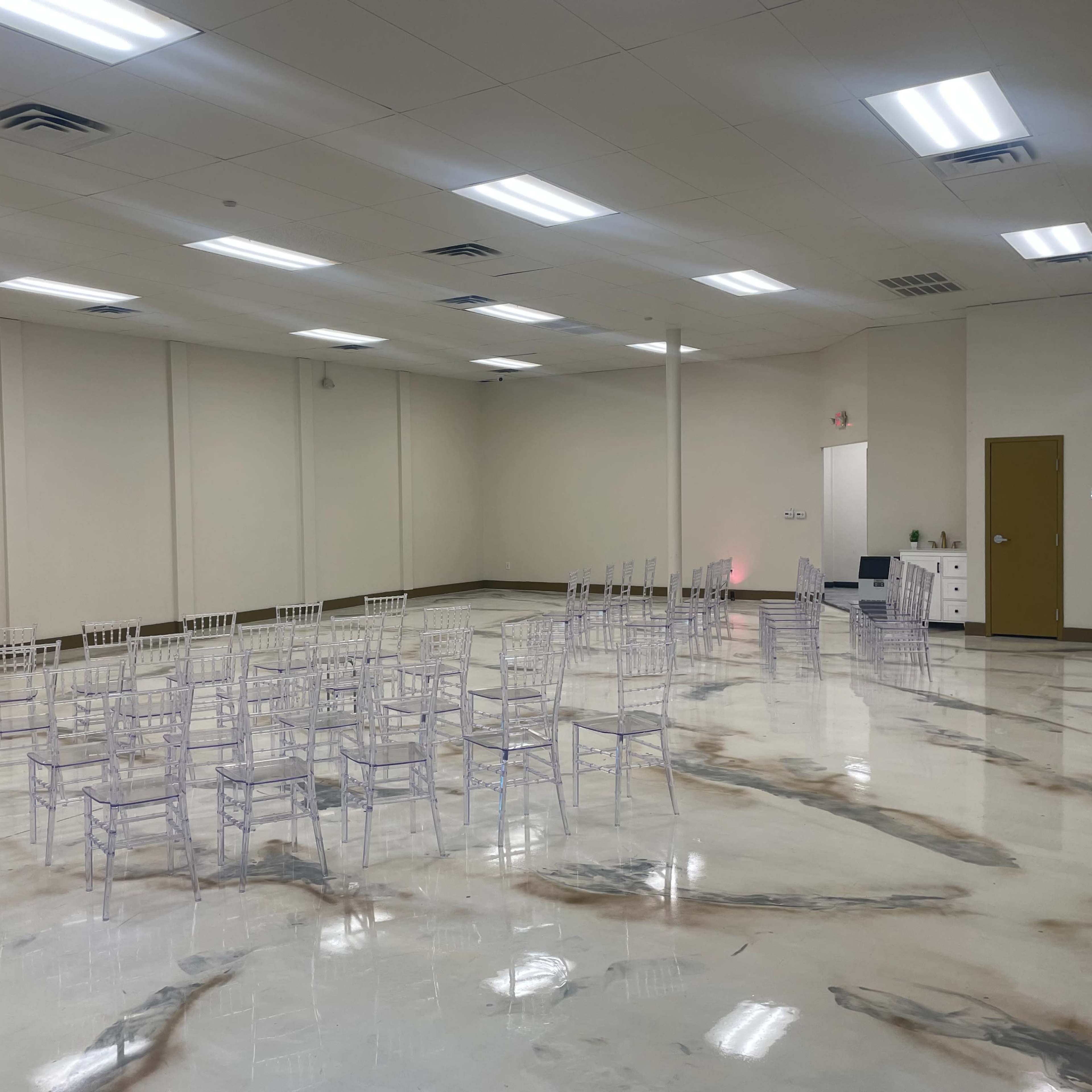 A large, empty room features rows of clear chairs on a polished, marbled floor.