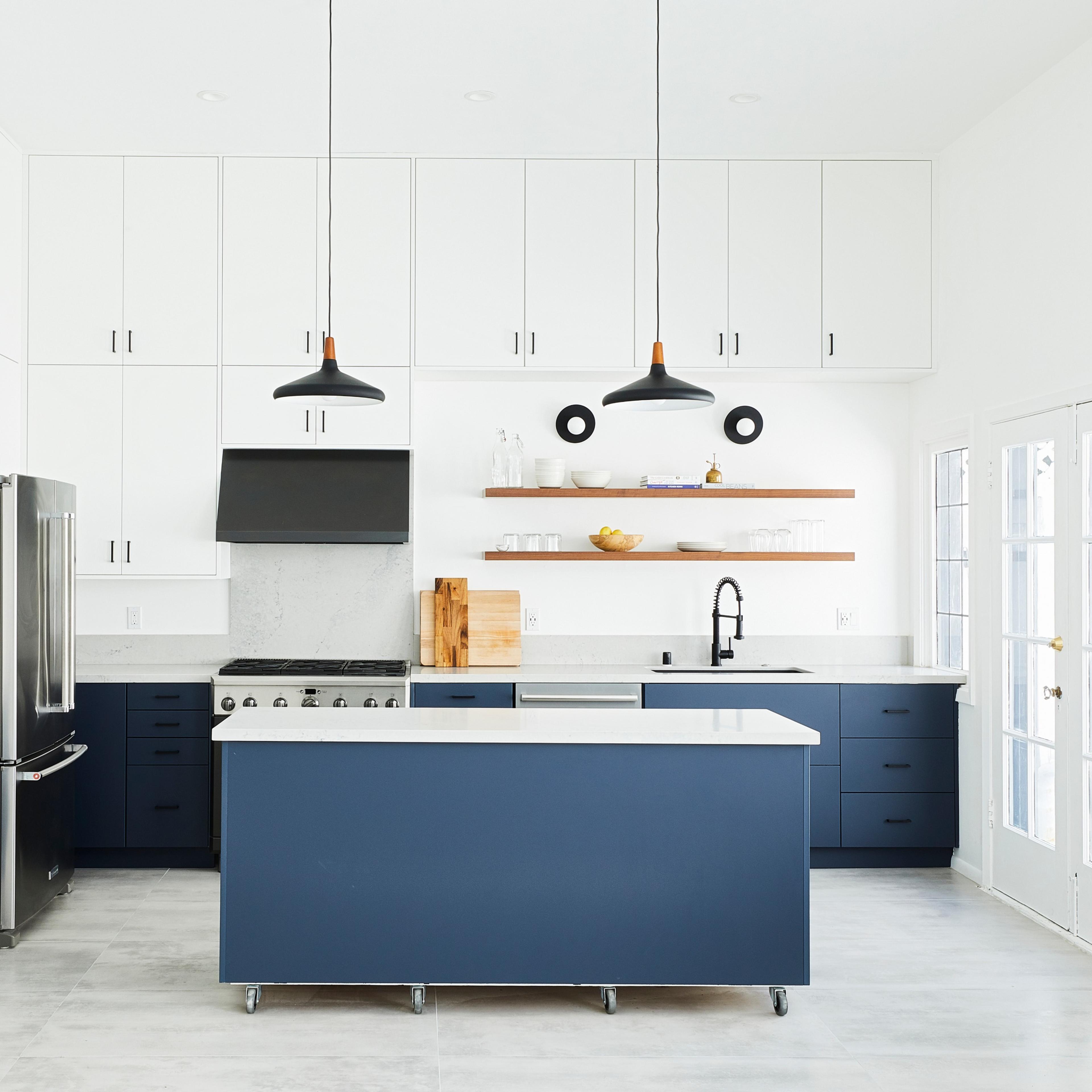A modern kitchen with white upper cabinets, navy blue lower cabinets, a large island, and stainless steel appliances.