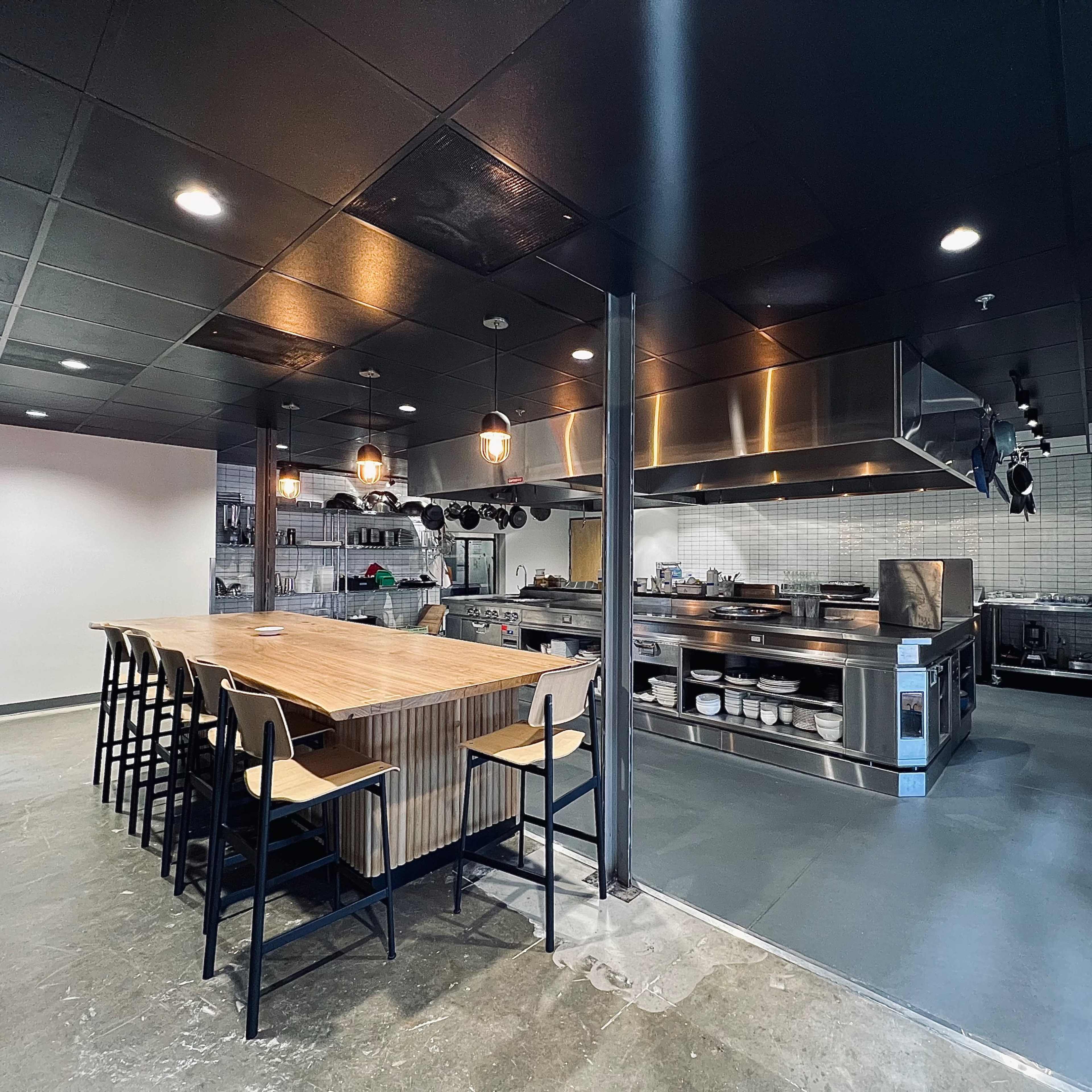 An industrial-style kitchen featuring a large wooden table and various stainless steel appliances.