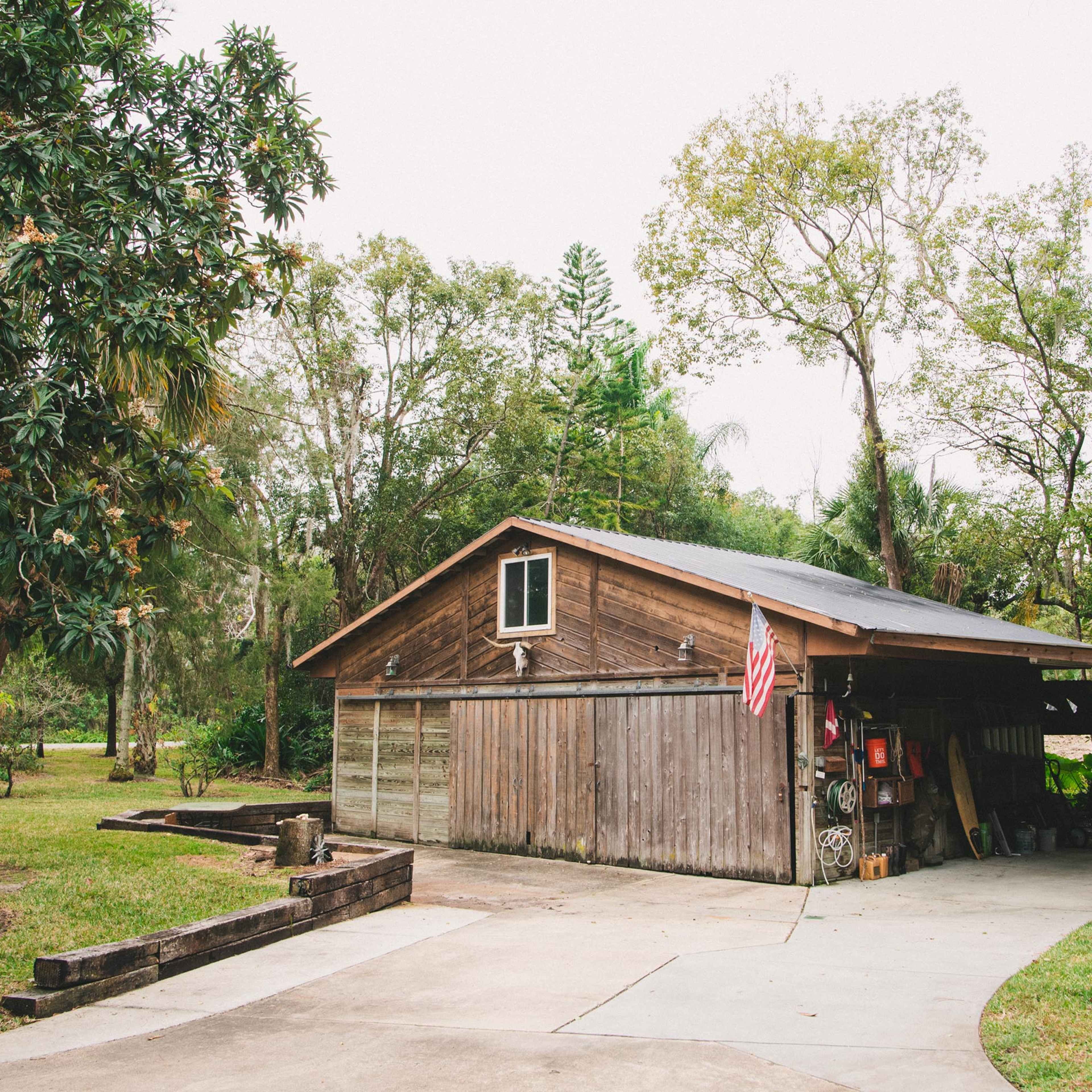 A wooden house with a covered porch is surrounded by trees and greenery in a rural setting.