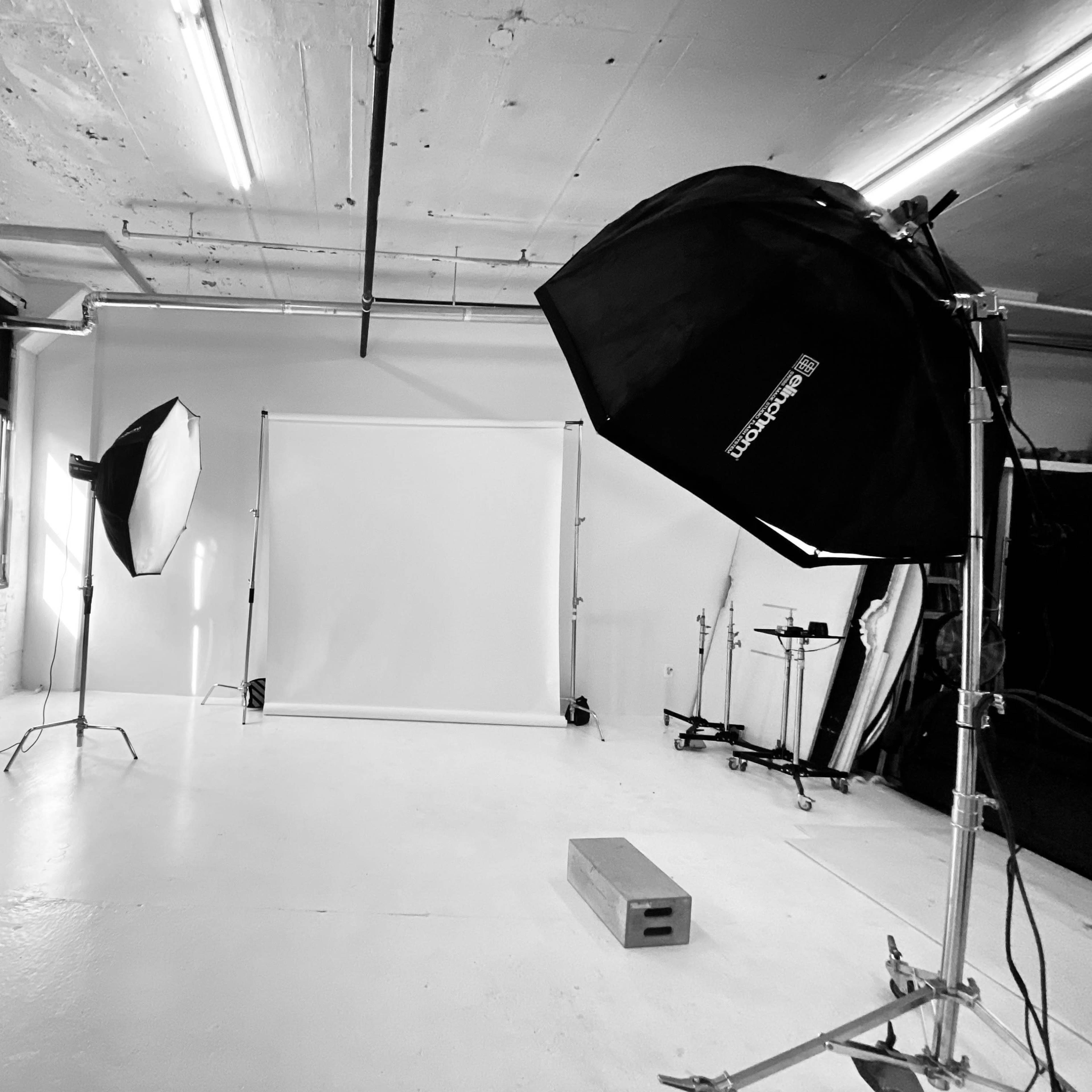 A photography studio with a blank backdrop, two lighting setups, and equipment arranged around a white floor.