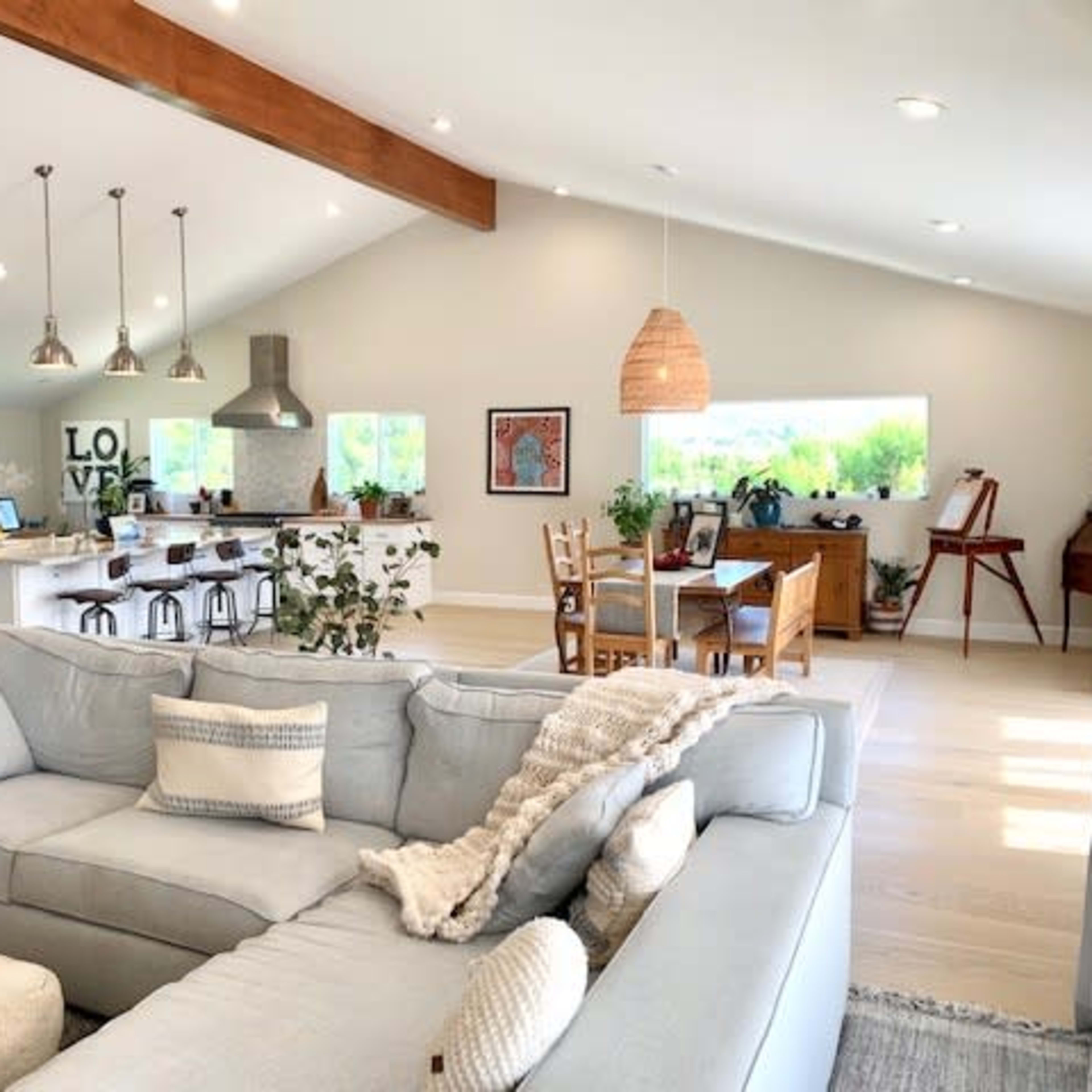 A spacious, modern living area features a light blue sectional sofa, a kitchen with stainless steel appliances, and a dining area with wooden furniture.