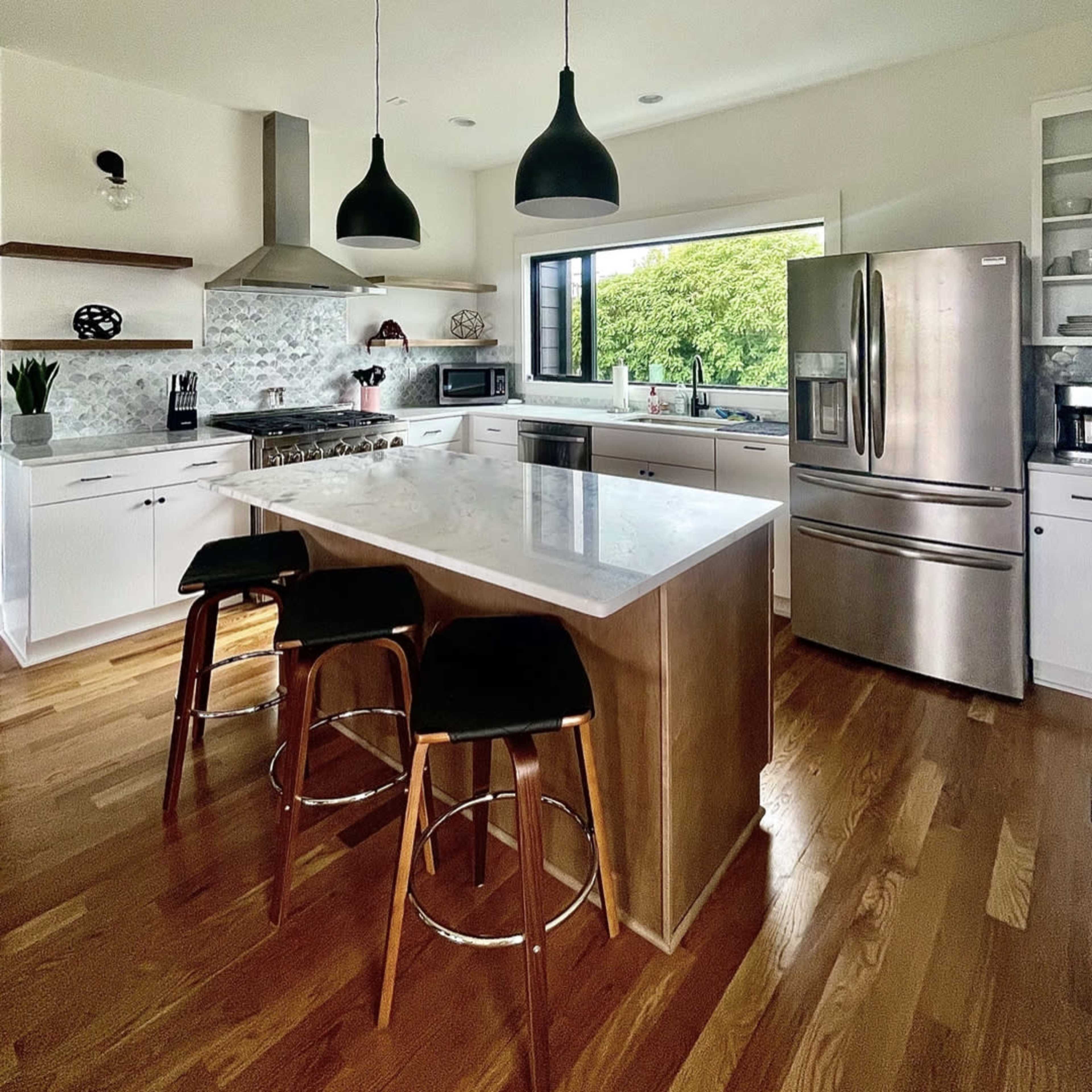 A modern kitchen features a central island with seating, stainless steel appliances, and ample natural light from a large window.