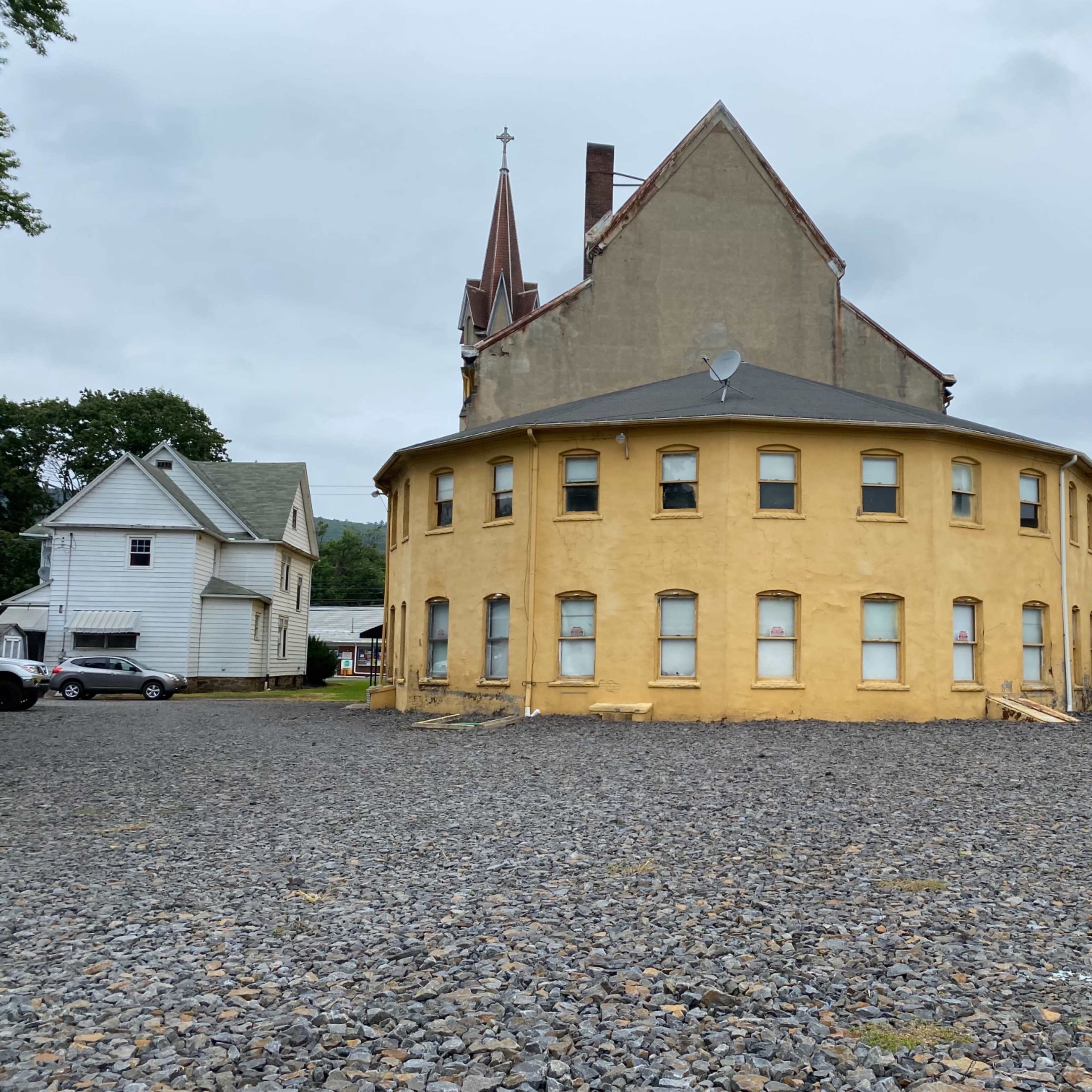 A circular, yellow building with multiple windows and a steeple in the background, set against a rocky terrain.