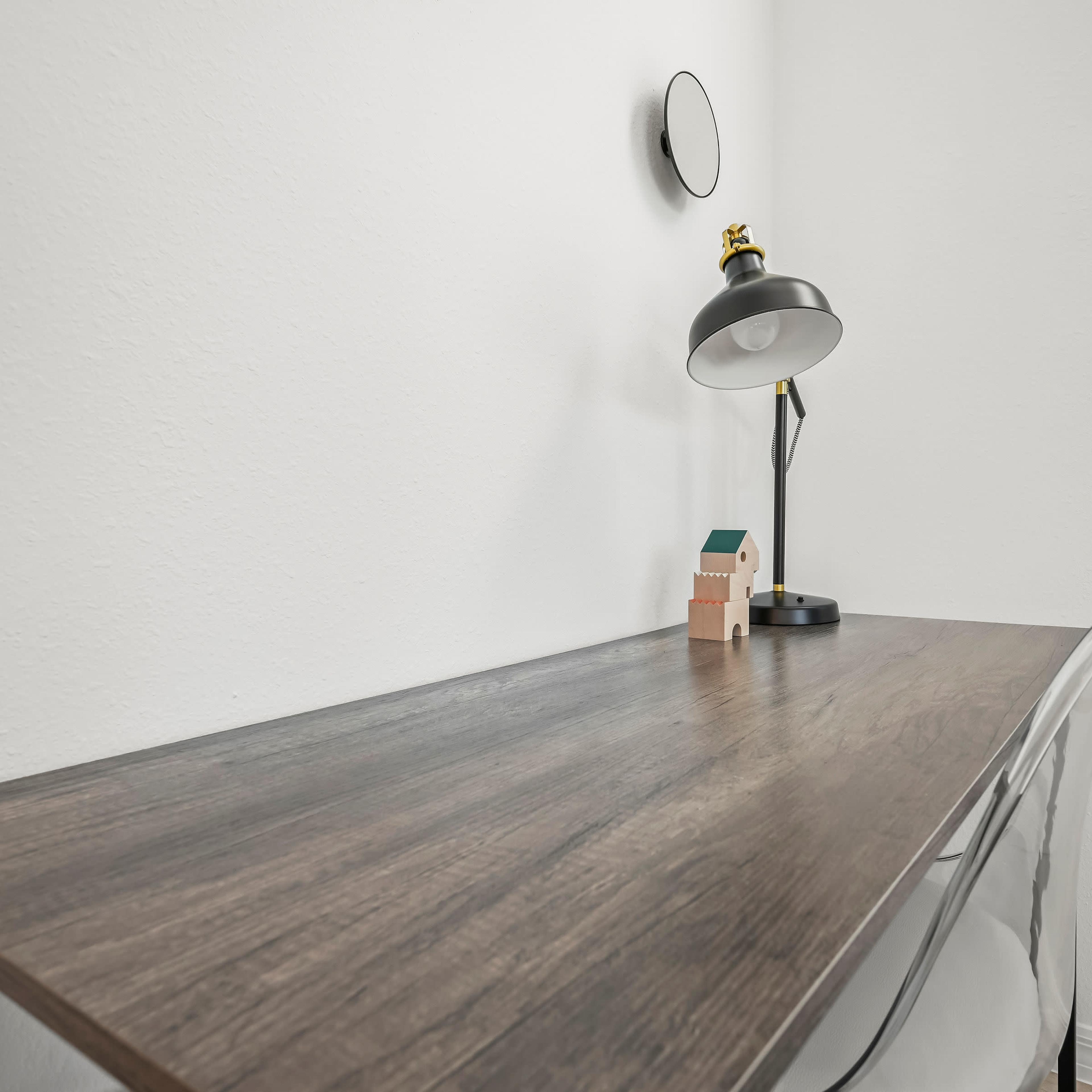 A clean wooden desk is positioned against a light-colored wall, featuring a modern lamp, a small decorative item, and a window with blinds.