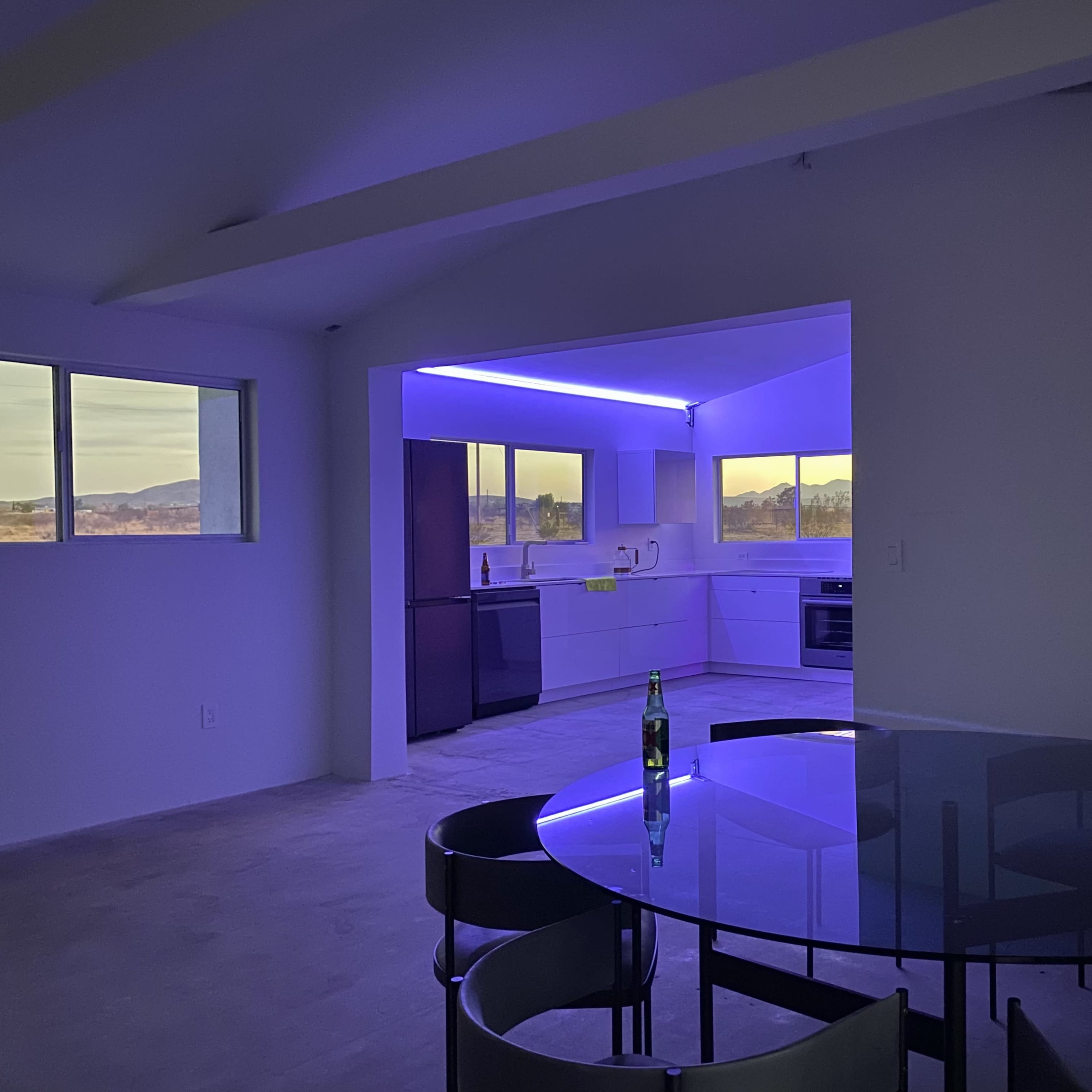 A minimalistic kitchen with modern appliances and a dining area featuring a round table, illuminated by purple lighting.