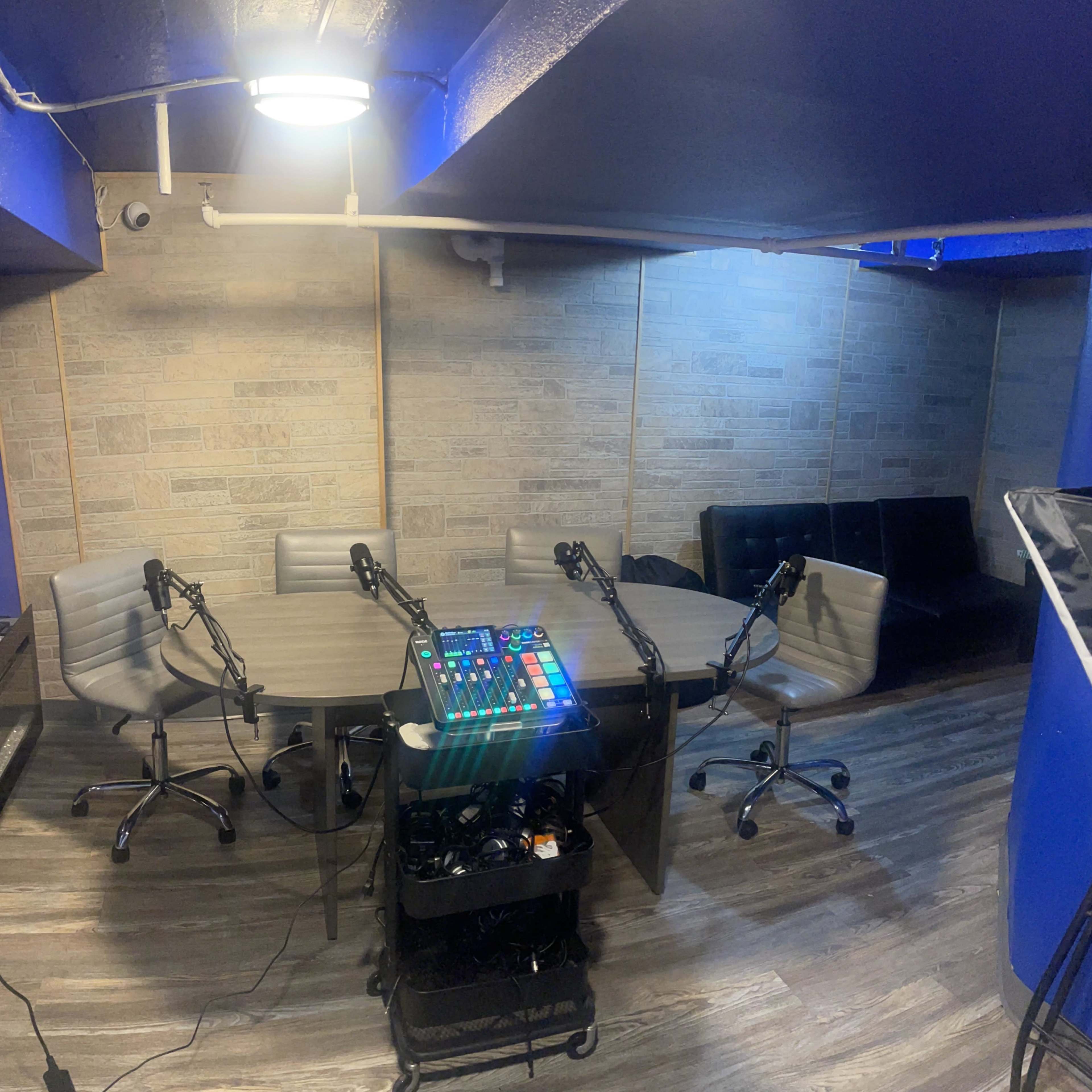 A recording studio with multiple microphones set up around a large oval table, surrounded by chairs, and a control panel on a cart.