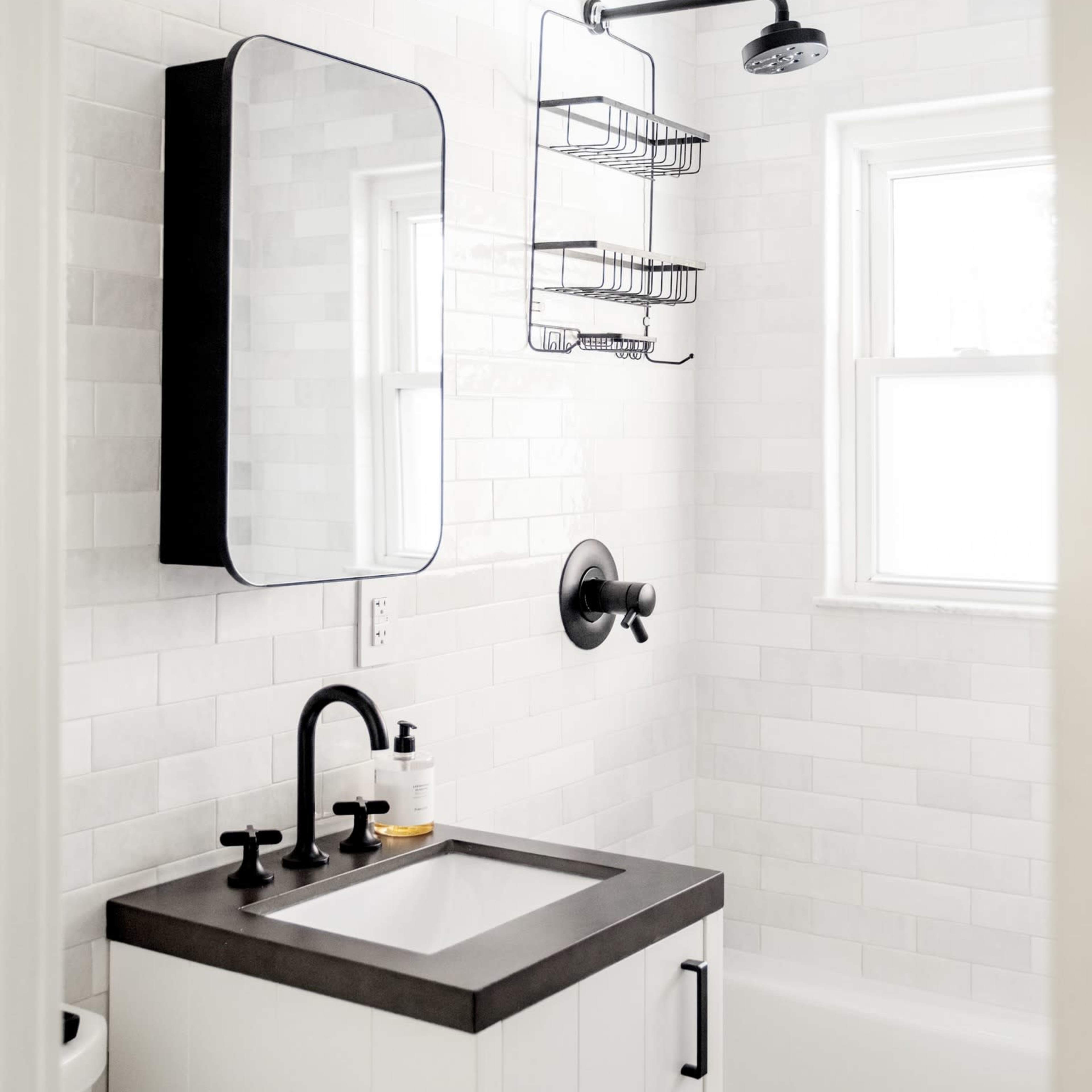 A compact bathroom features a wall-mounted mirror, a black shower head, and a wire rack for storage.