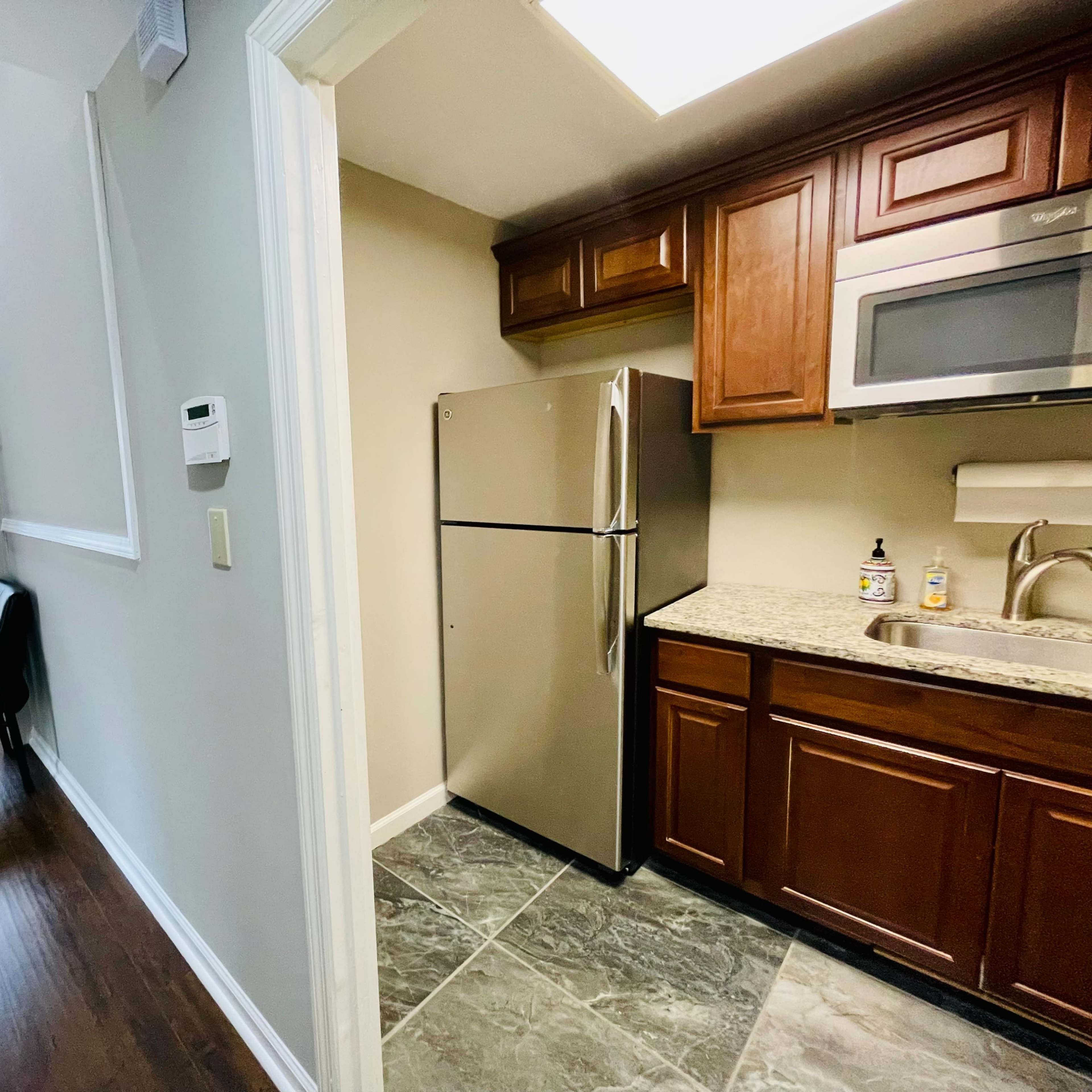 A kitchen area featuring stainless steel appliances and dark wooden cabinets, adjacent to a small hallway with a chair and a window.
