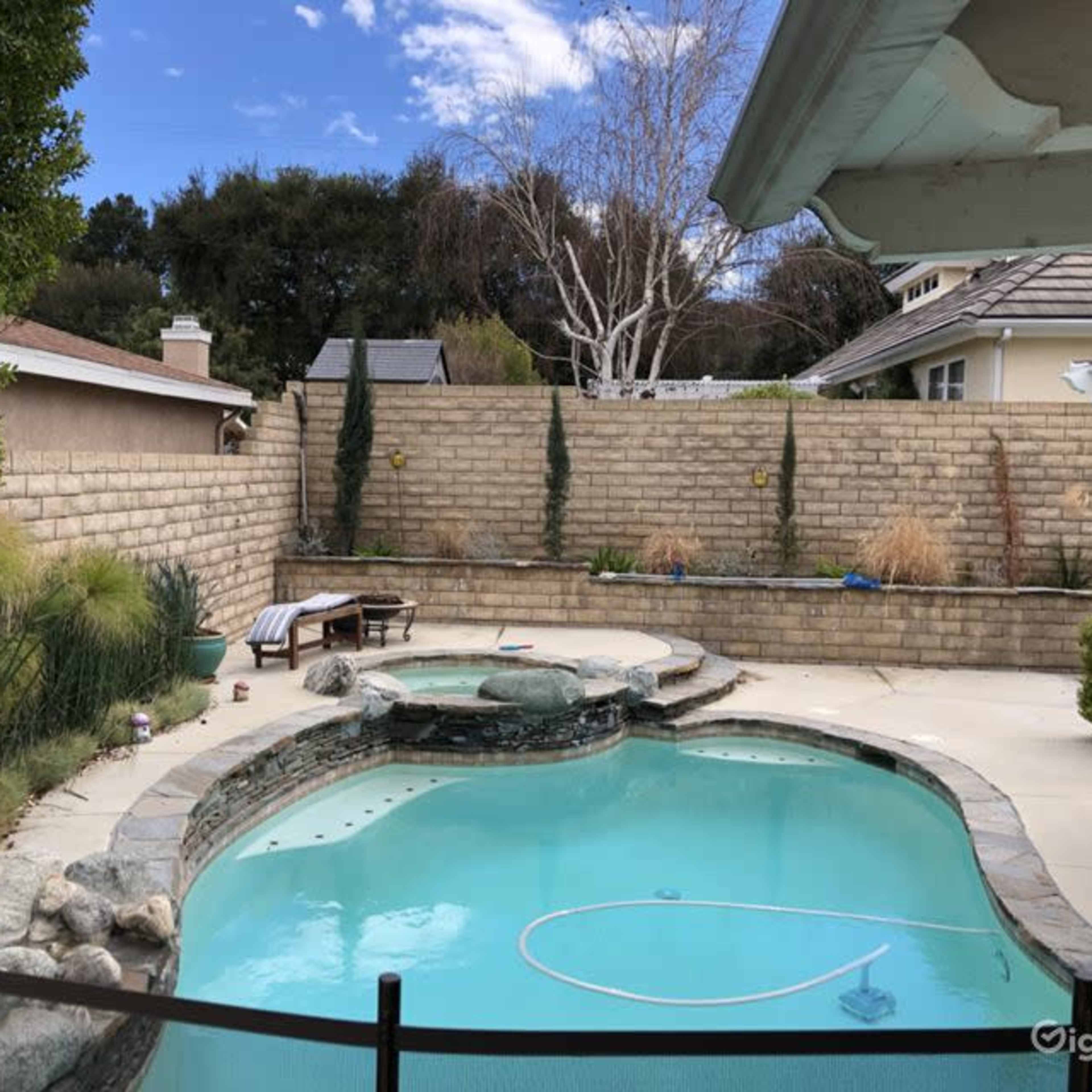A backyard pool area surrounded by a stone wall, with landscaping elements and a clear blue sky.