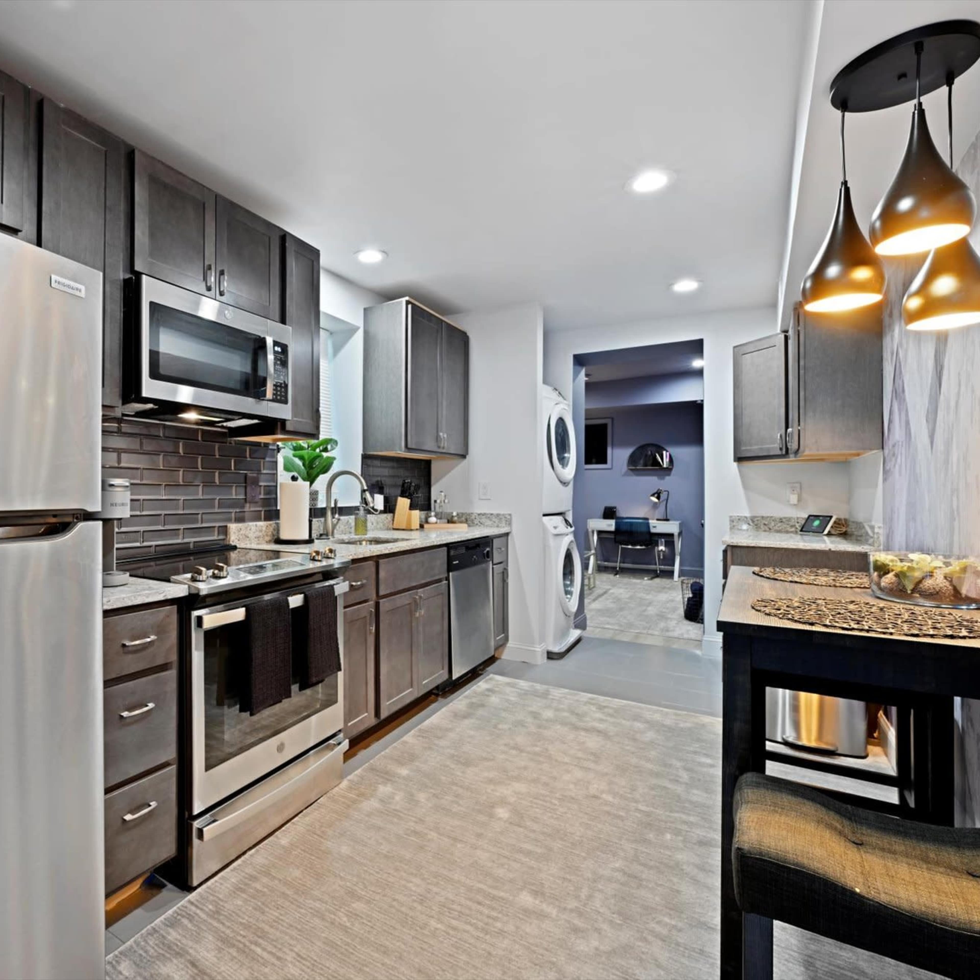 A modern kitchen featuring stainless steel appliances, dark cabinetry, and a light-colored countertop.