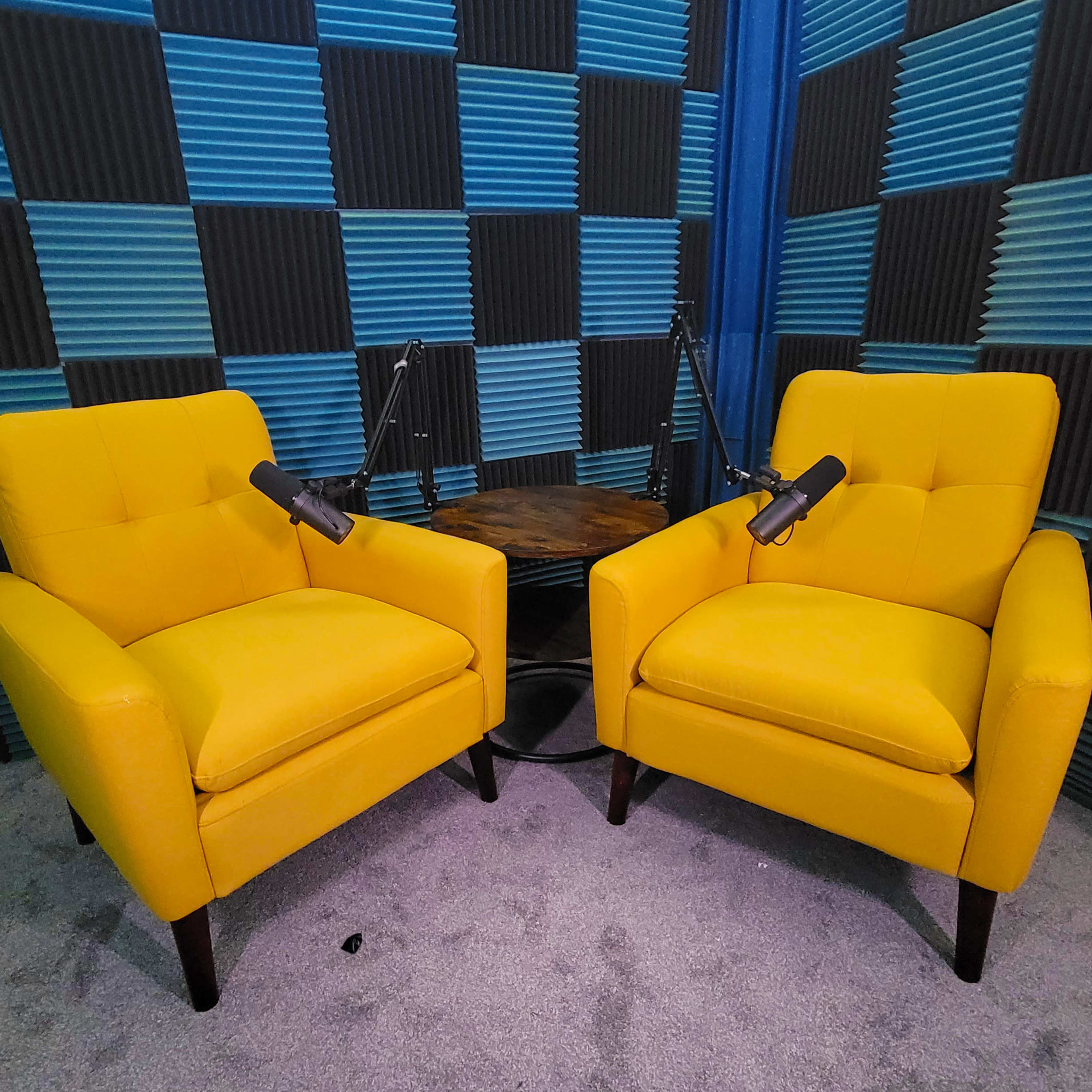 Two yellow armchairs facing each other, positioned next to a small wooden table, with soundproofing foam panels in shades of blue and black in the background.