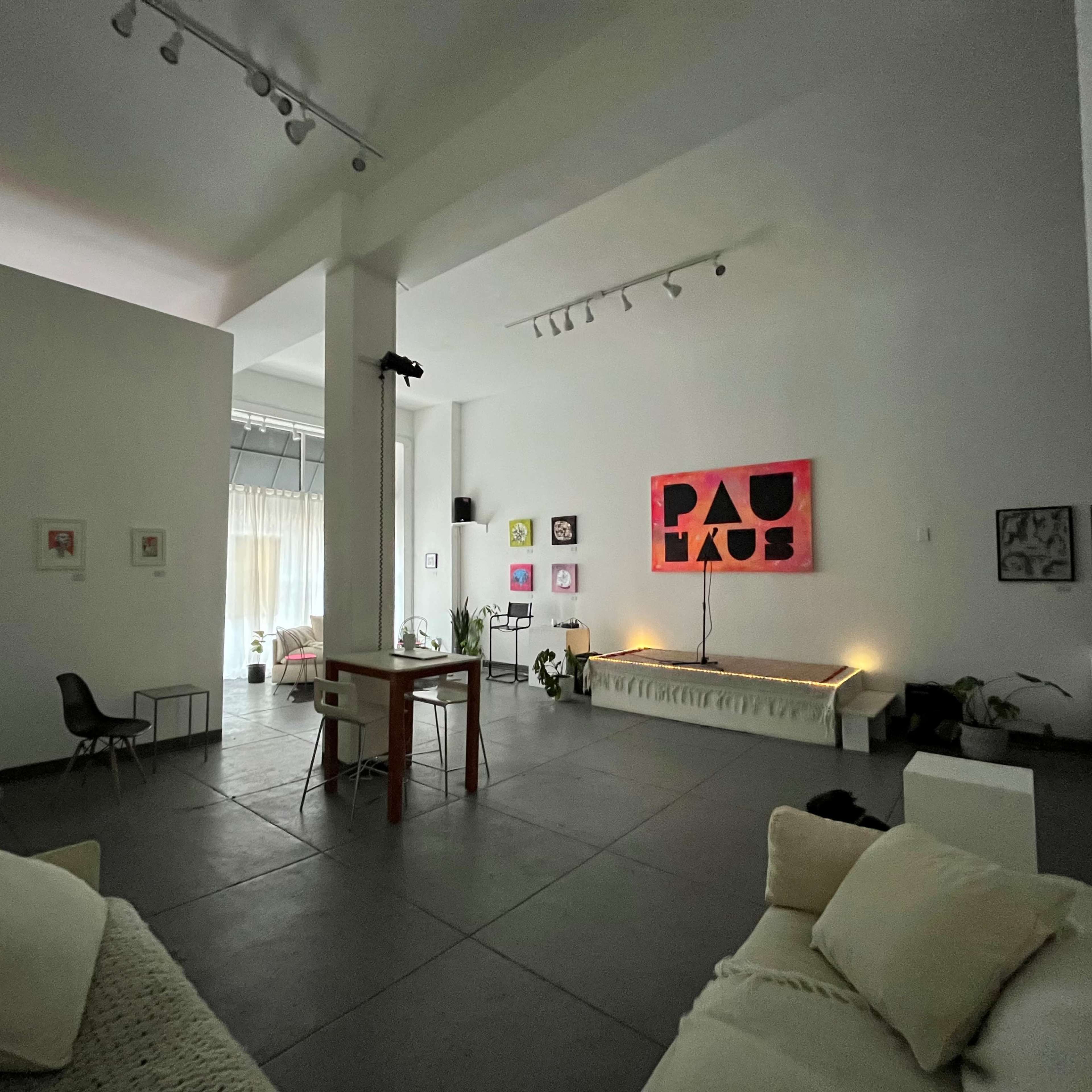 A spacious, modern art studio featuring a mix of seating, a long bench, and various artworks displayed on the white walls.