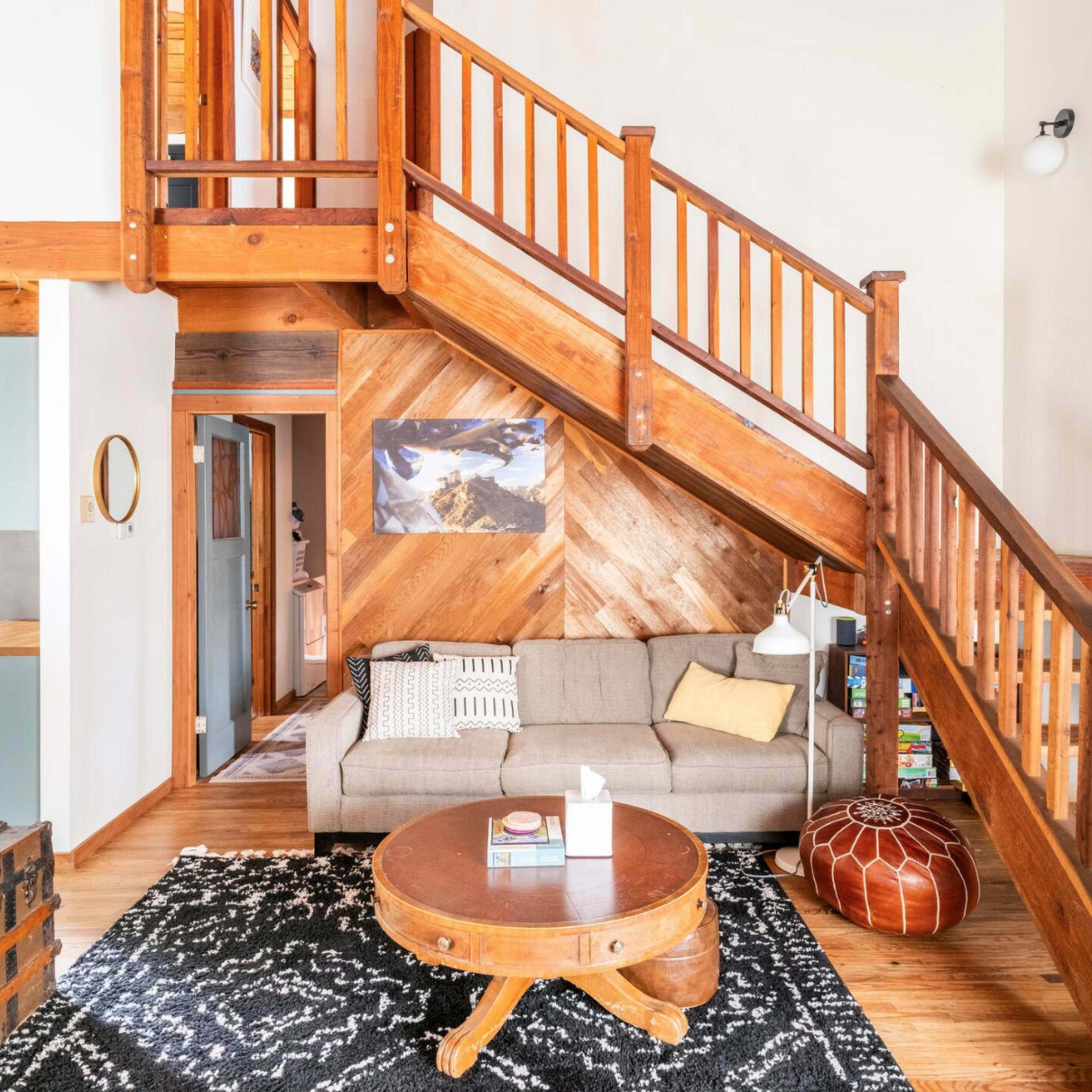 A spacious living room with a wooden staircase, a couch, a round coffee table, and a patterned rug.