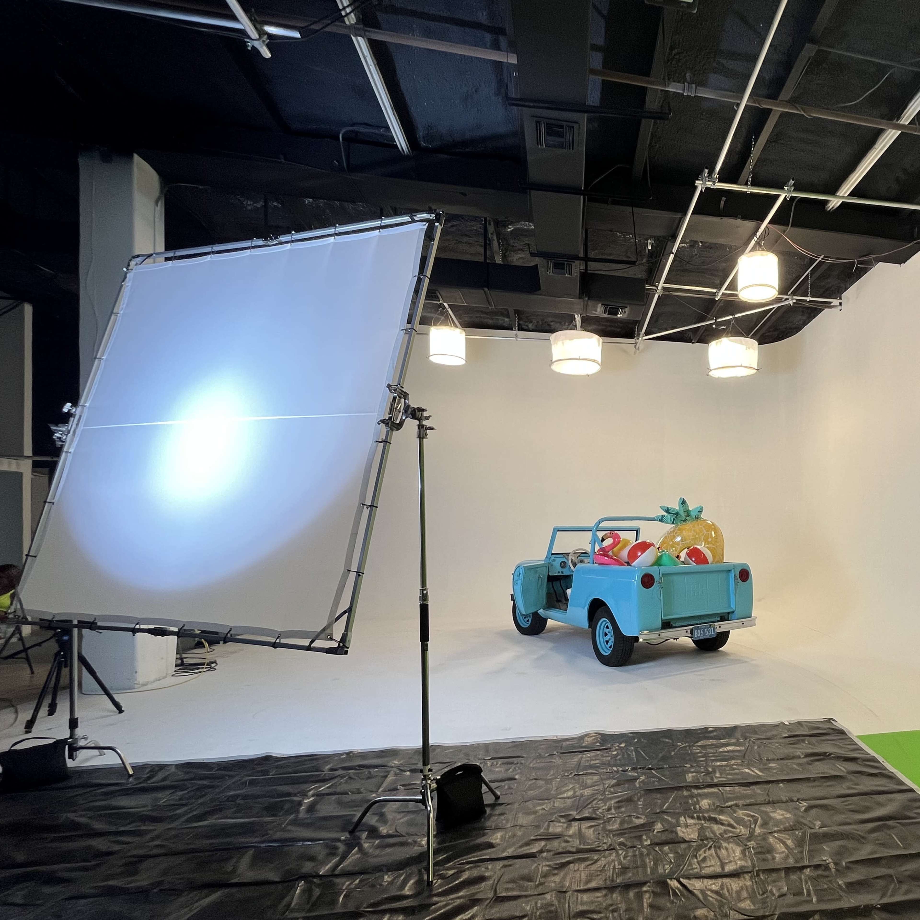 A light blue car filled with inflatable beach toys is positioned in a studio with a white backdrop and lighting setup.