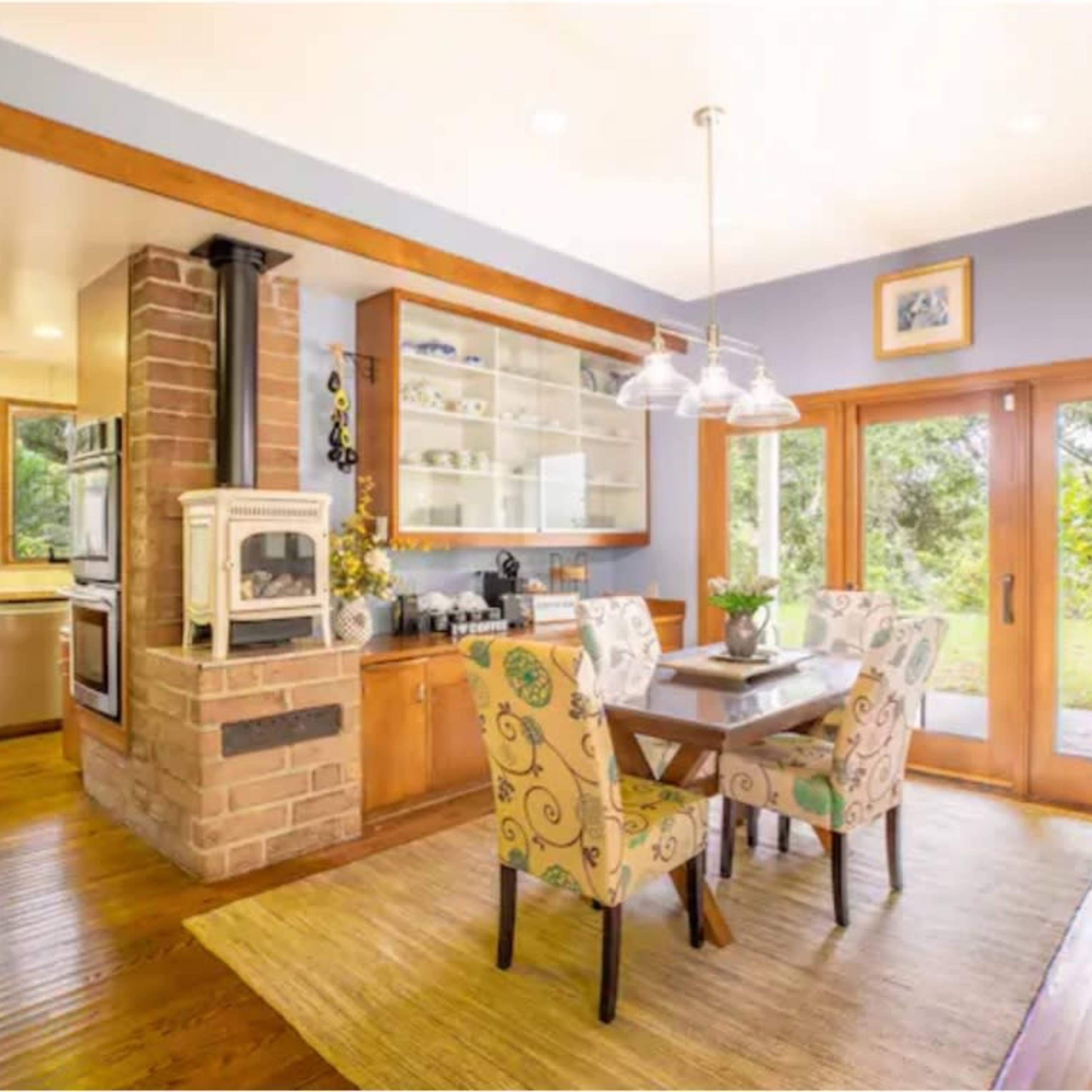 A dining area features a table with decorative chairs, surrounded by large windows and wooden cabinetry.
