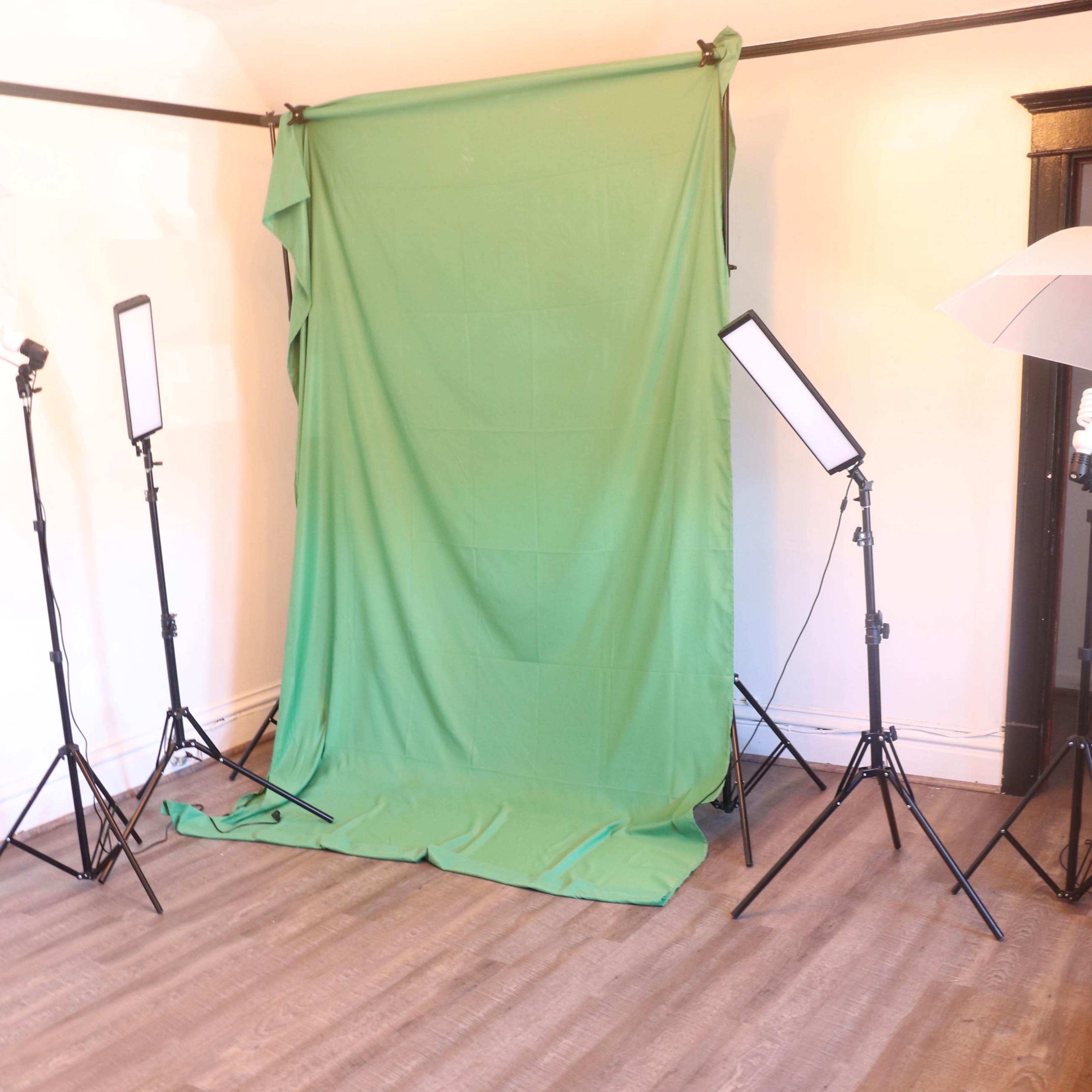 A photo studio setup featuring a green backdrop, two softbox lights, and a wooden floor.