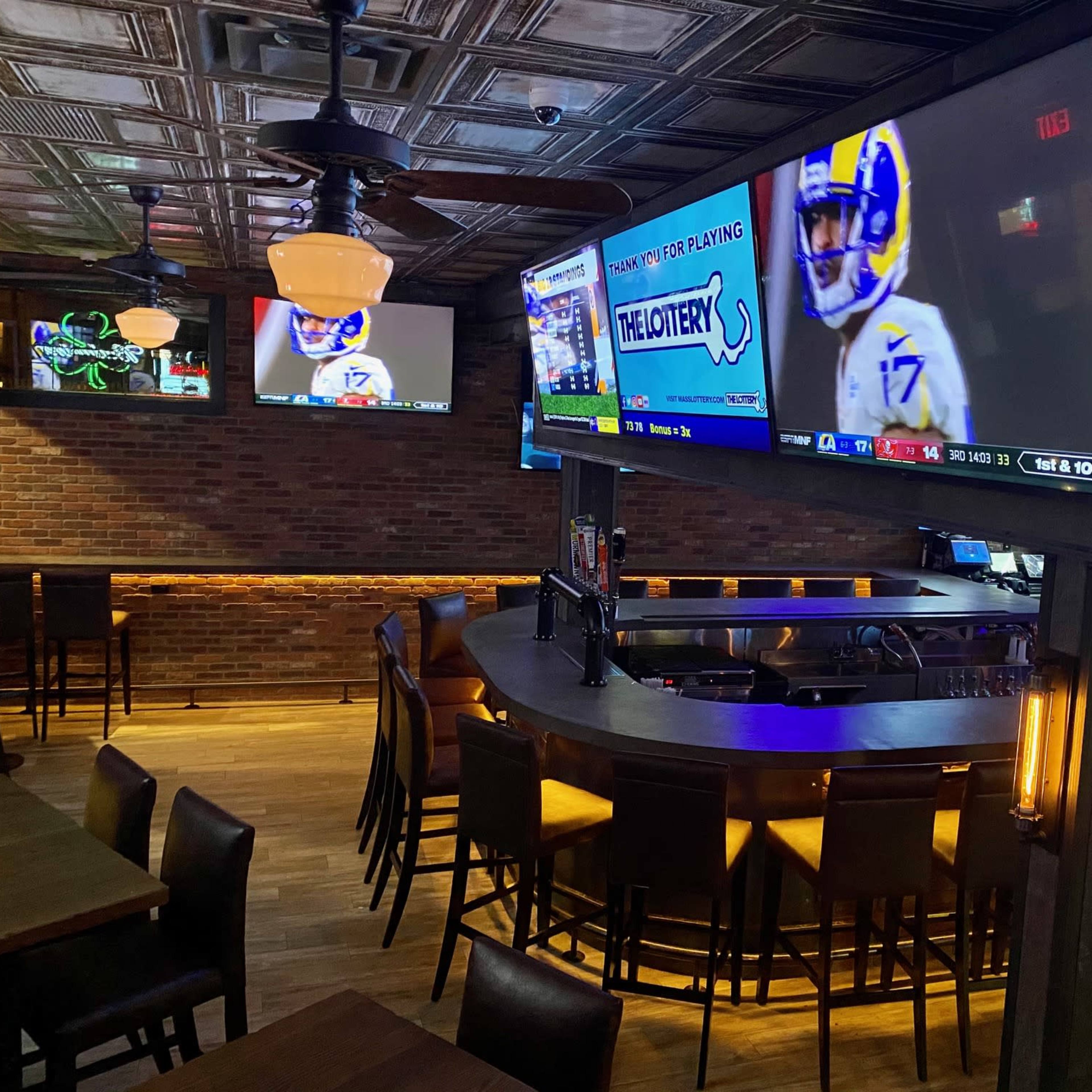 A bar interior with a curved counter, several tables, and multiple large TVs displaying sports events on the walls.