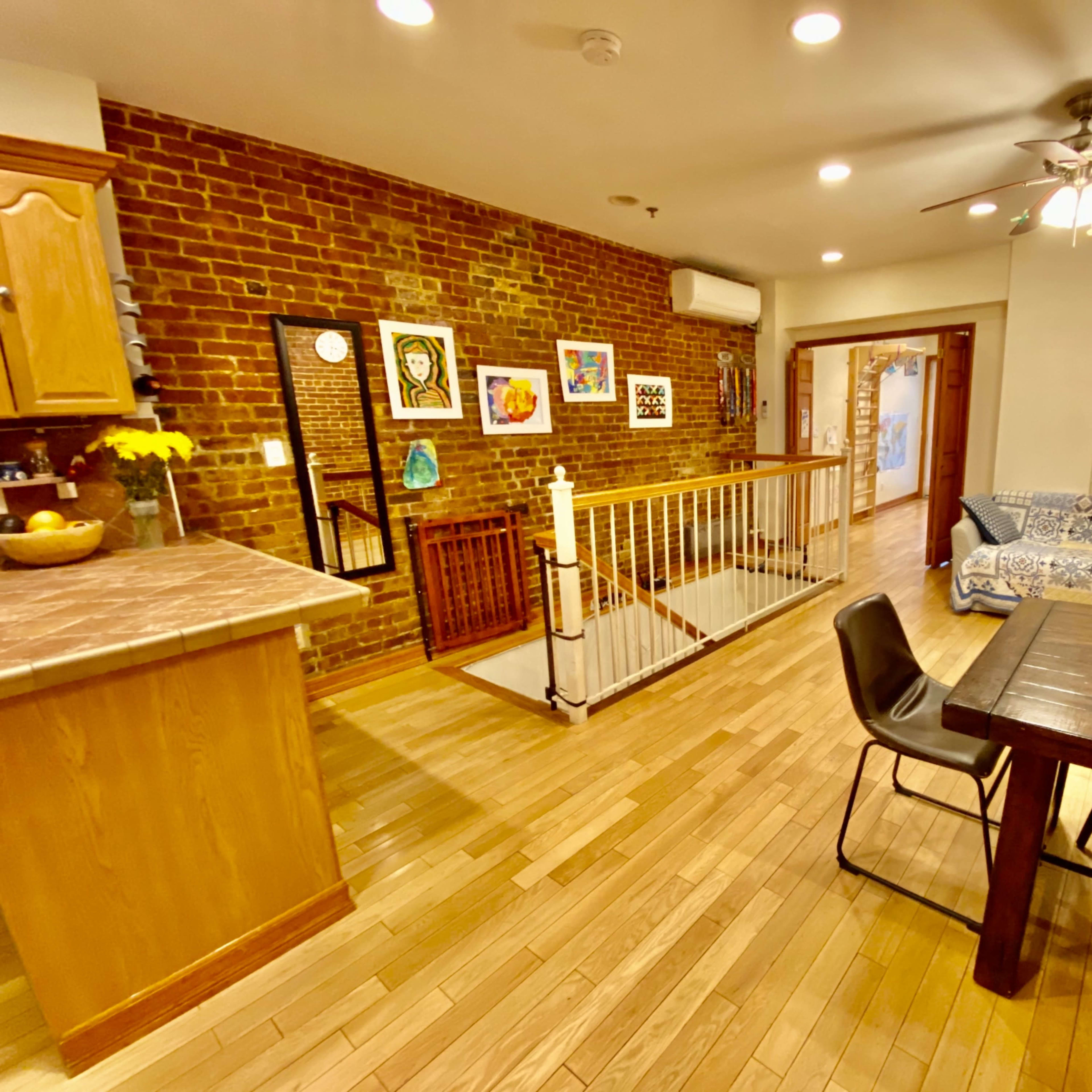 An open-concept living space featuring a kitchen area with wooden cabinets, a dining table, a seating area with a couch, and exposed brick walls.