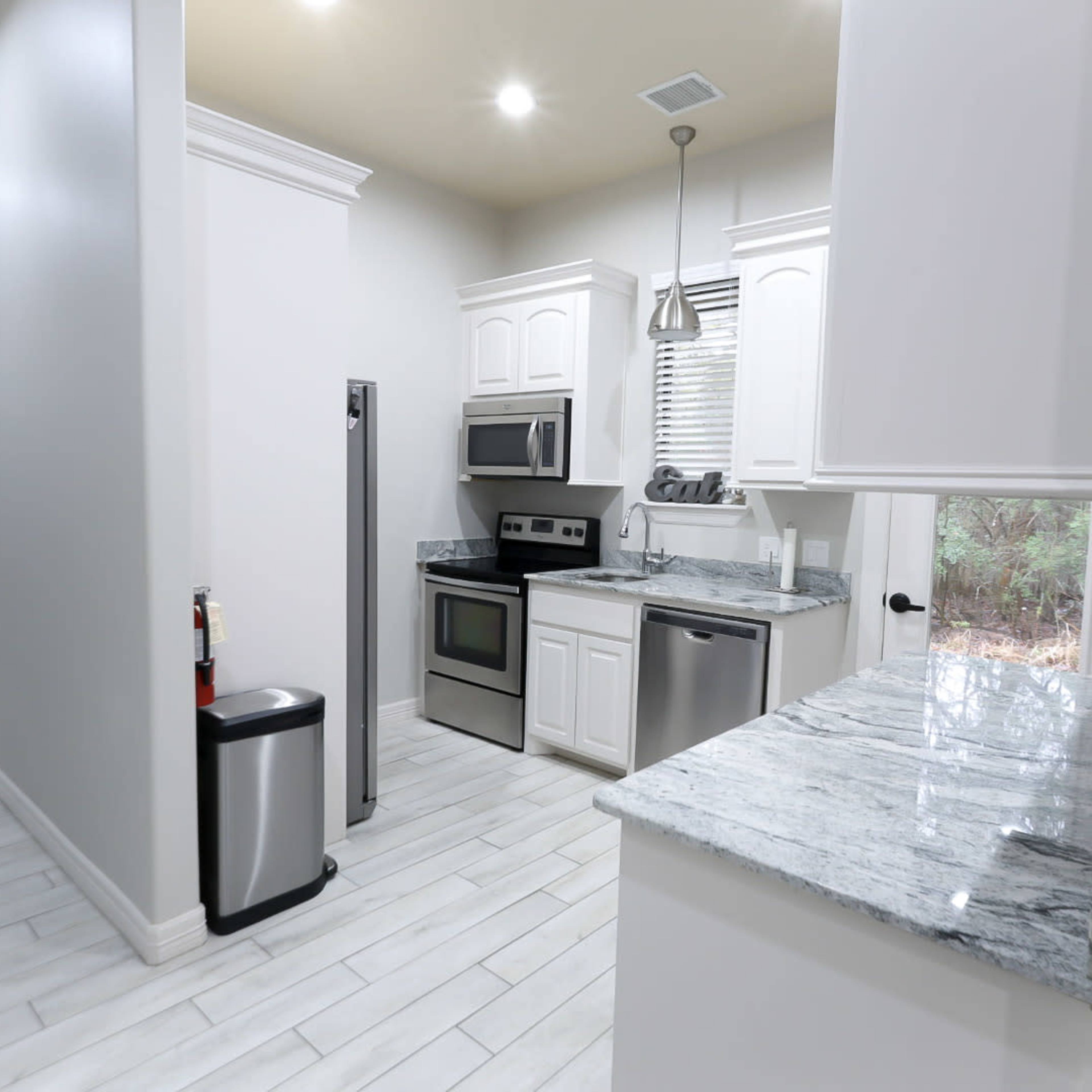 A modern kitchen featuring white cabinetry, stainless steel appliances, and a marble countertop.