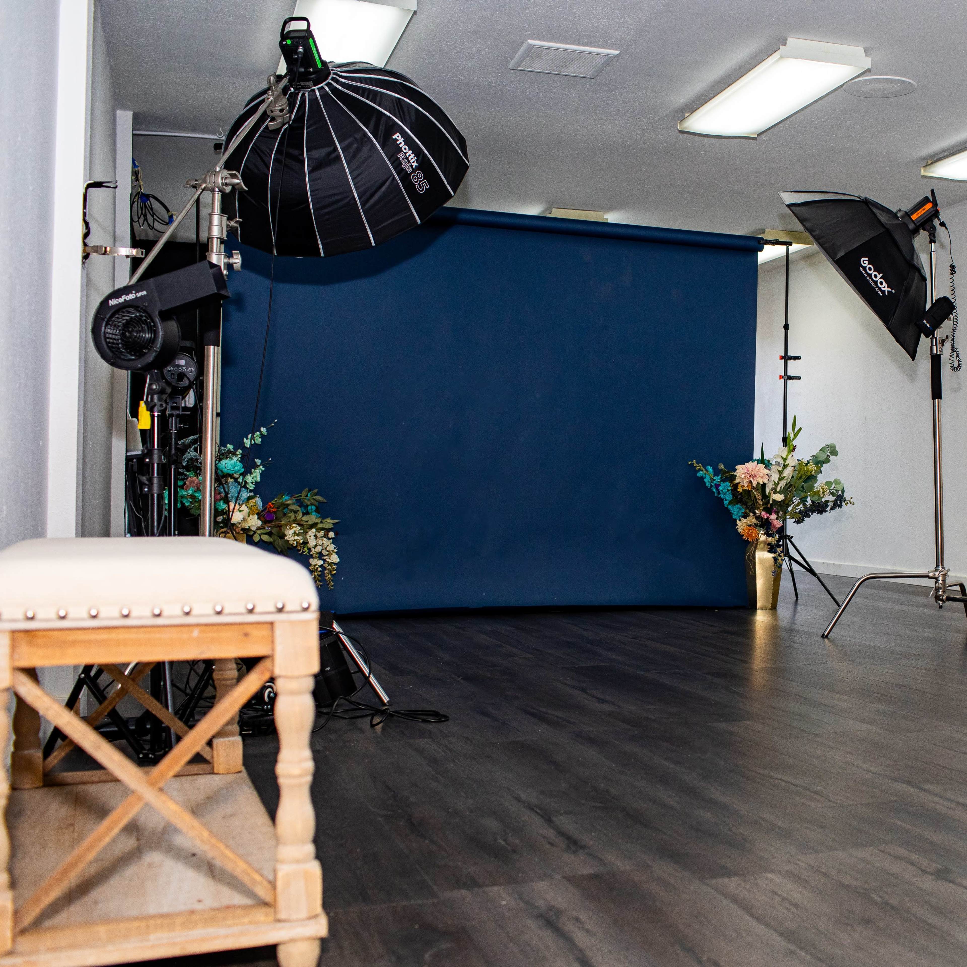 A photography studio featuring a blue backdrop, several lighting equipment setups, and minimal decor.