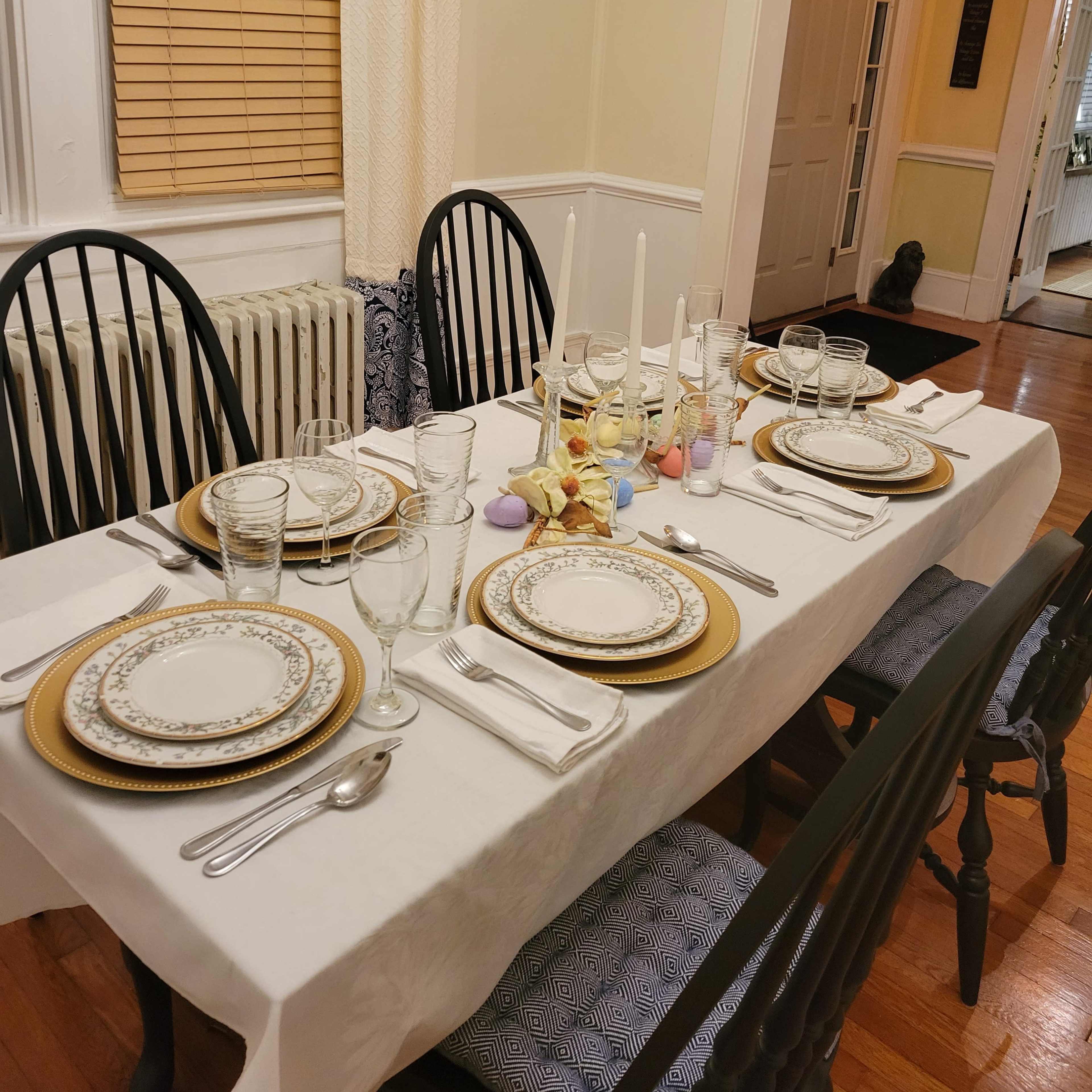 A dining table is set with plates, glassware, and cutlery, arranged neatly for a meal in a well-lit room with a doorway leading to another area.