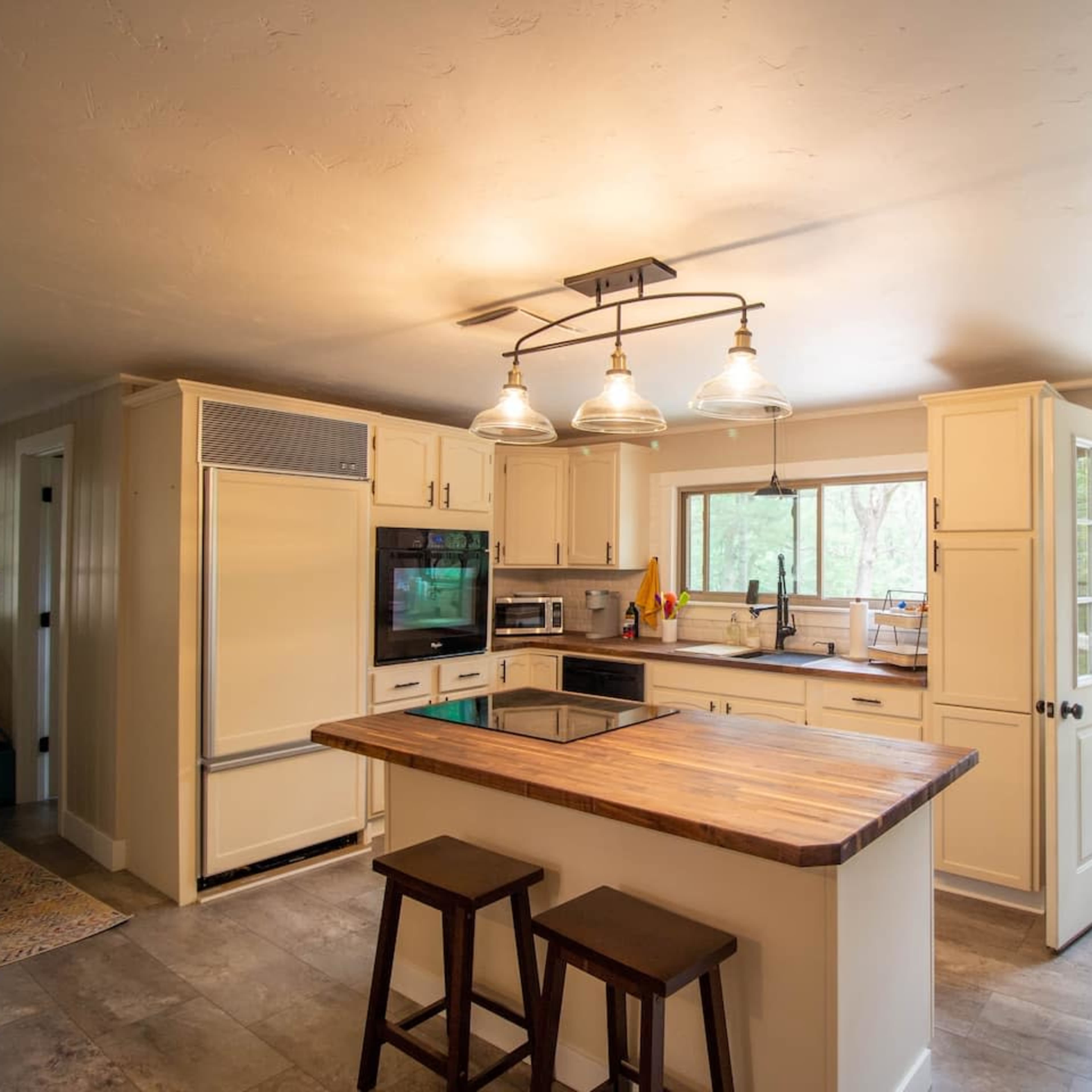 A modern kitchen with a central island, wooden countertops, and a doorway leading to an outdoor area.