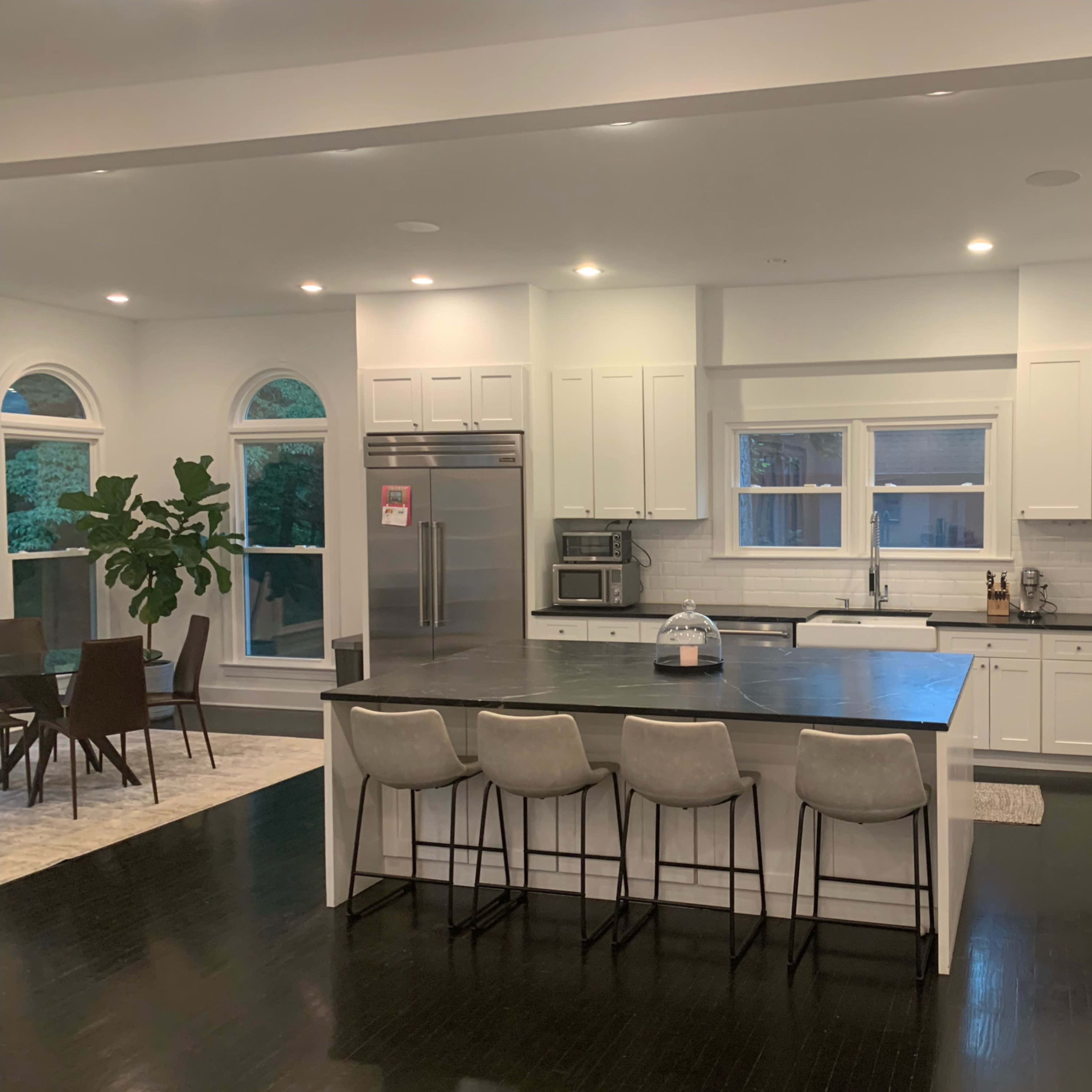 A modern kitchen features a large island with four stools, stainless steel appliances, and a view of a dining area with a table and chairs.