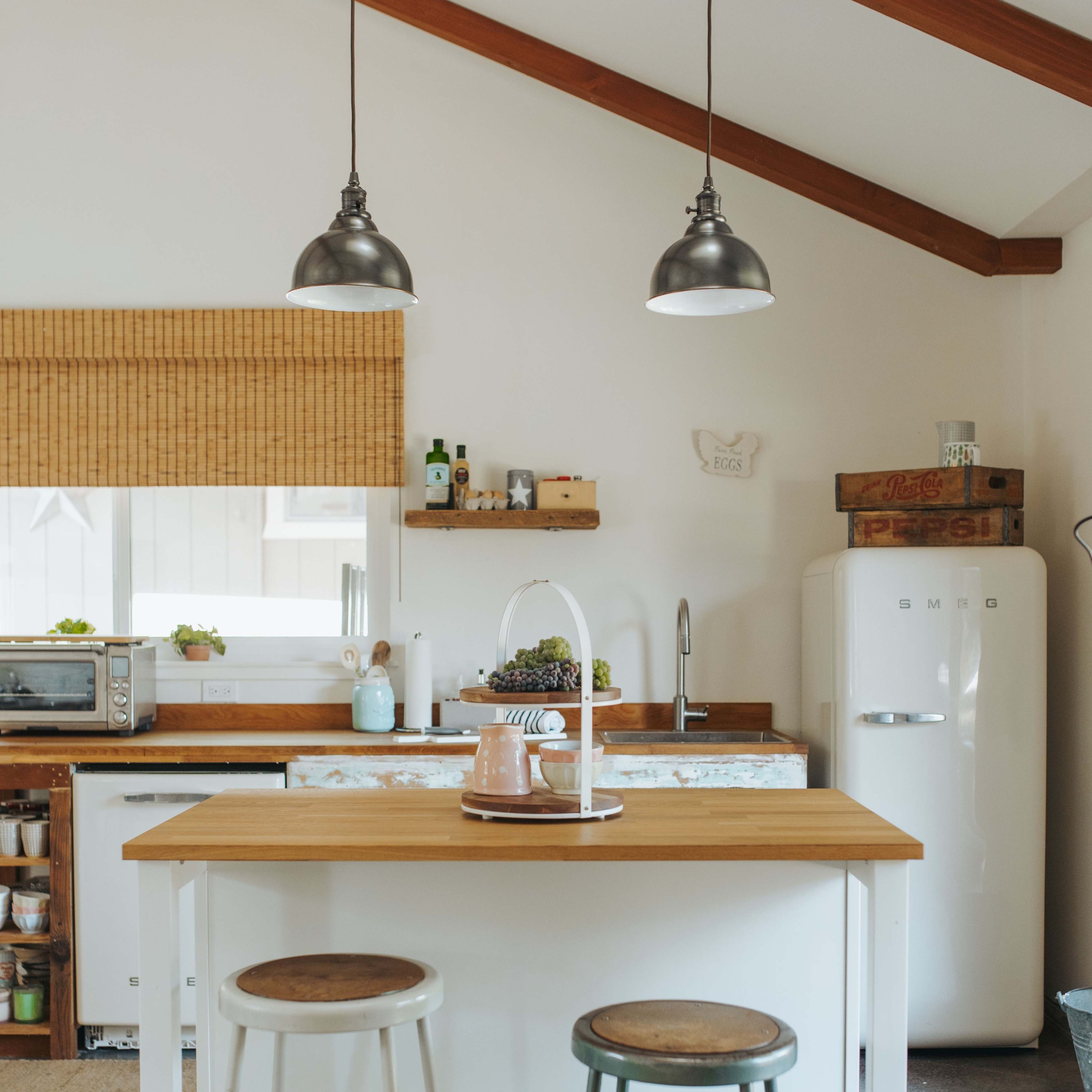 The kitchen features a wooden island with two stools, pendant lights hanging from a sloped ceiling, and a vintage refrigerator in the background.