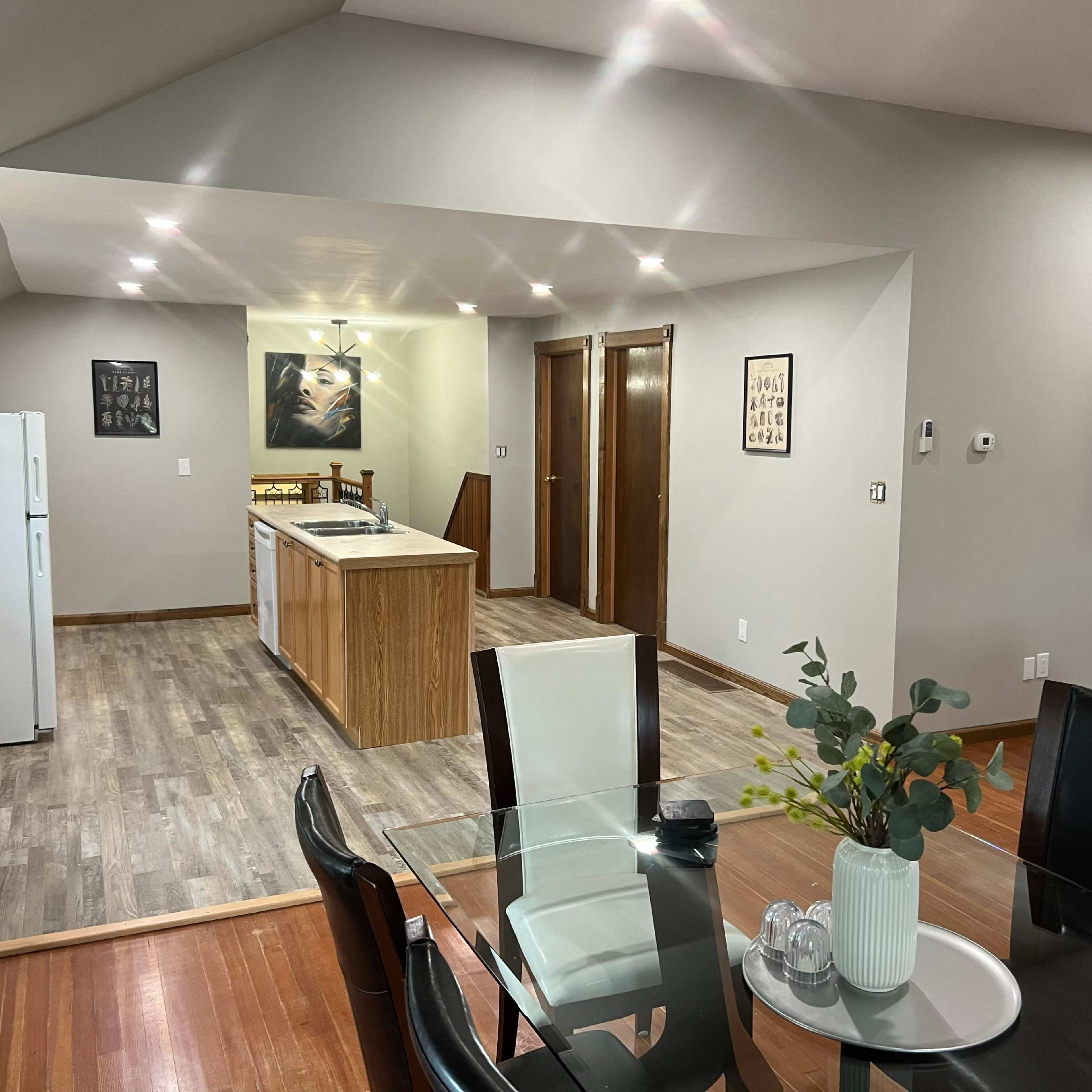 A modern kitchen and dining area with a table, chairs, and an island, featuring wood and neutral-colored walls and flooring.