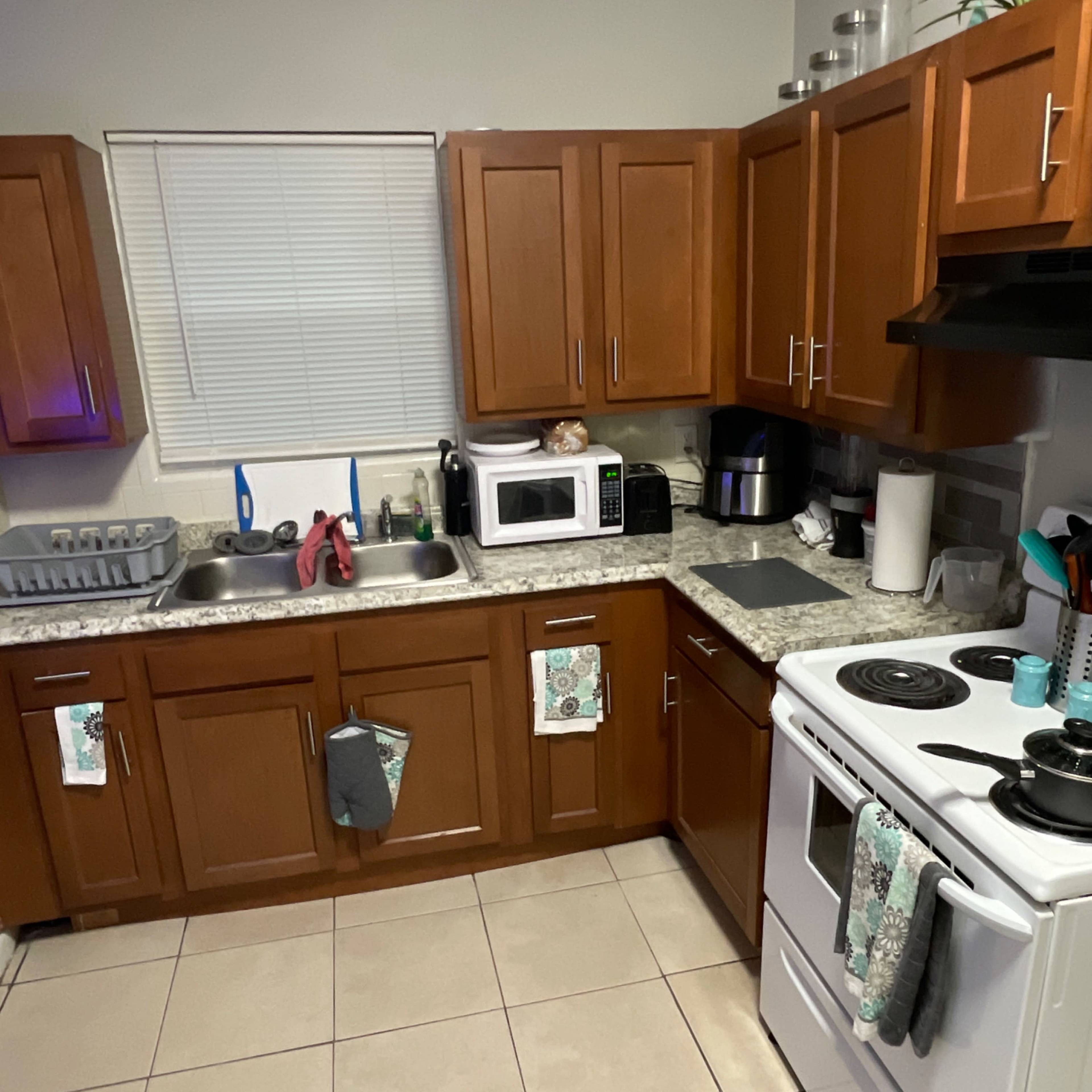 A kitchen with wooden cabinets, a countertop featuring a sink, microwave, and stove, along with various kitchen utensils and appliances.