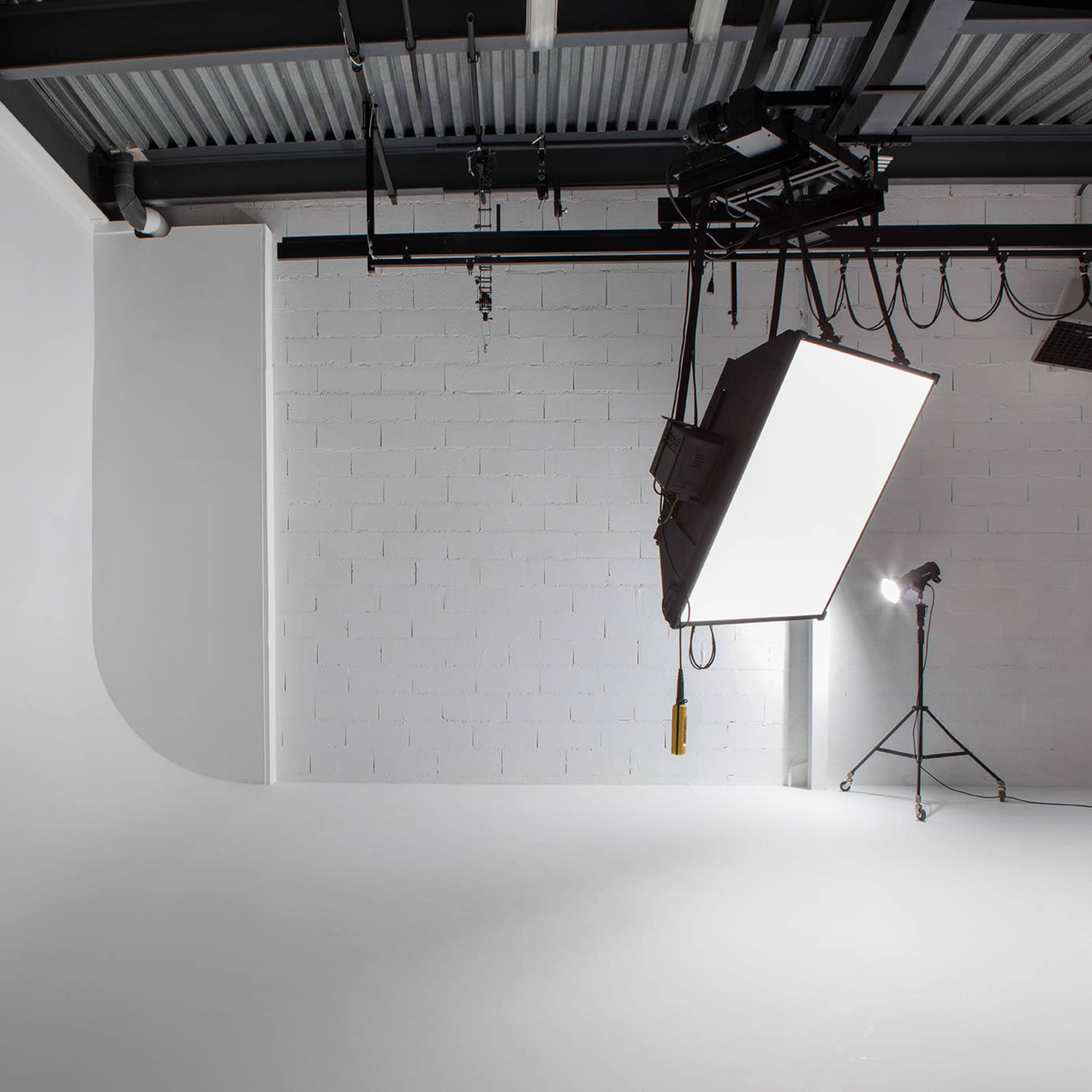 A minimalistic photography studio with a curved white backdrop and overhead lighting equipment.