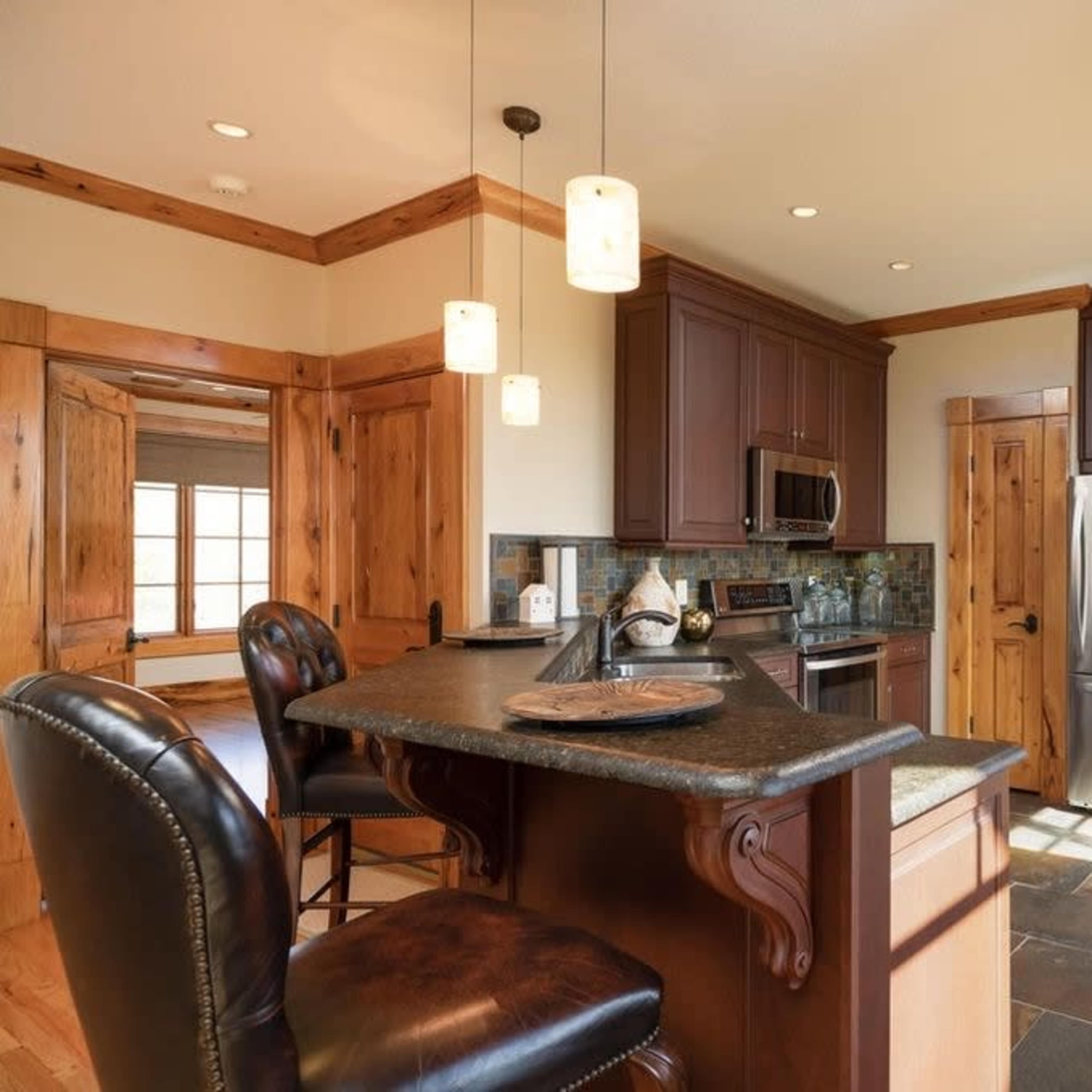 A modern kitchen featuring dark wooden cabinets, stainless steel appliances, and a stone countertop with seating at the bar.