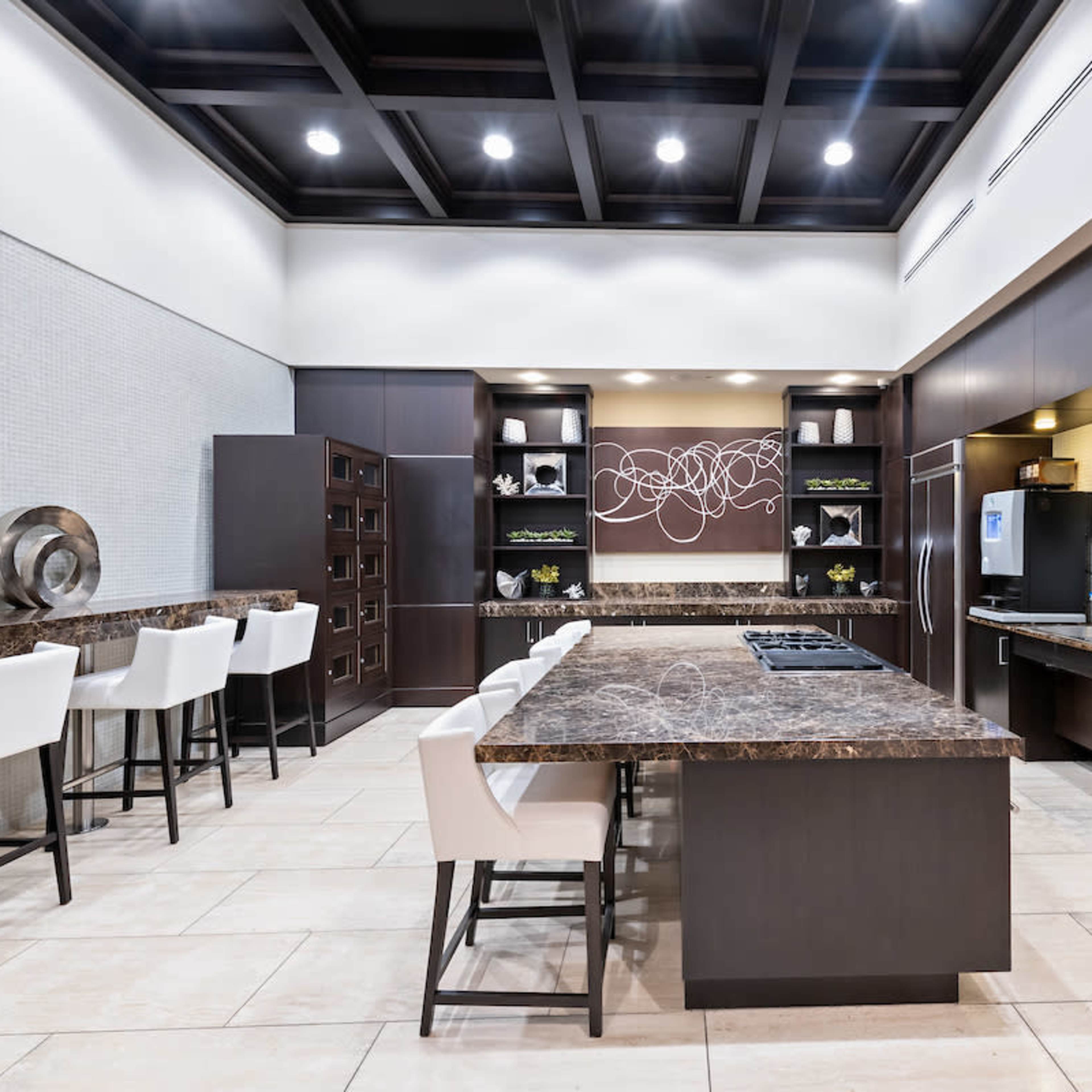 A modern kitchen featuring dark cabinetry, a large island with a marble countertop, and bar seating.