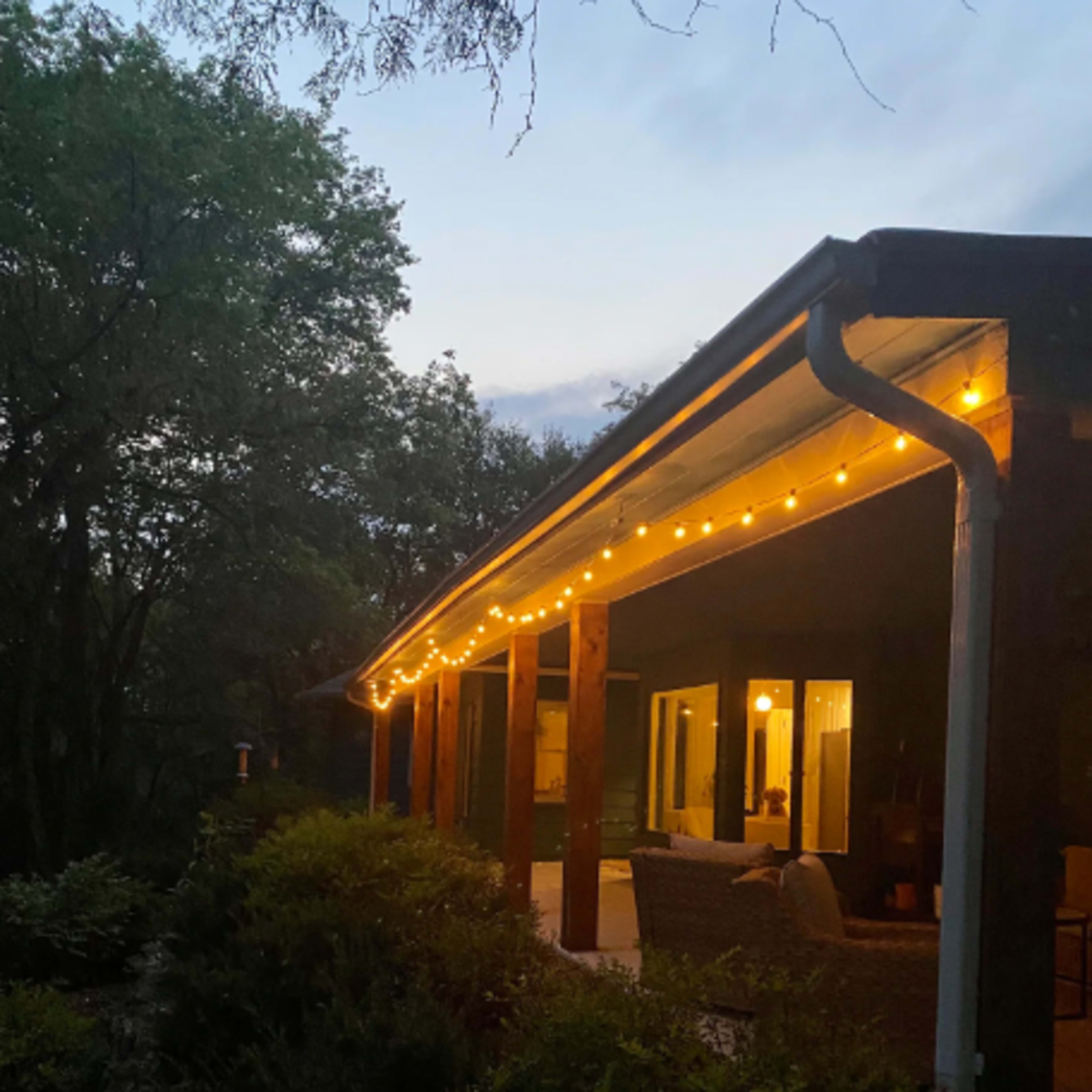 A house exterior with warm string lights along the porch, surrounded by trees at twilight.