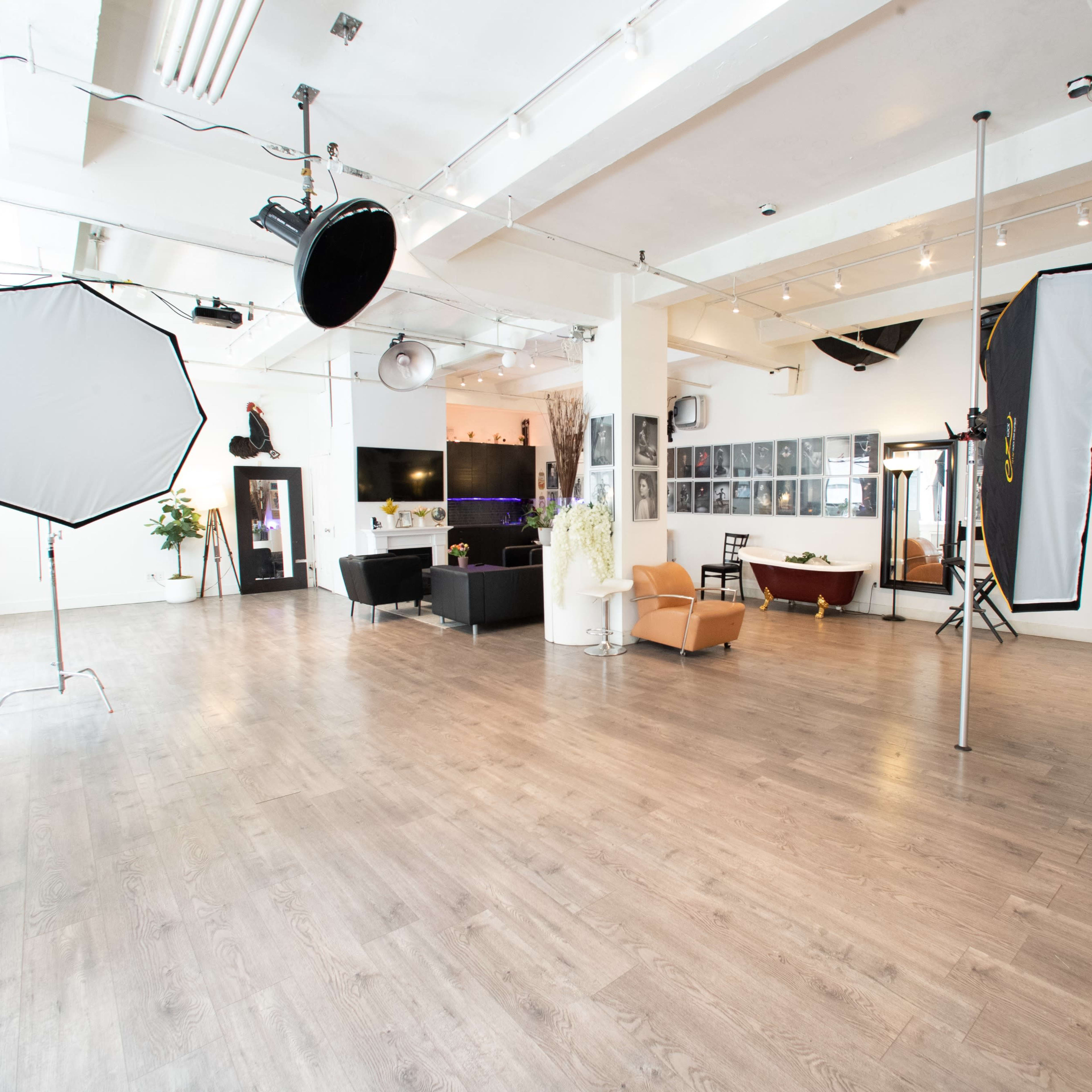 A spacious, well-lit photography studio featuring various lighting equipment, seating areas, and decorative plants.