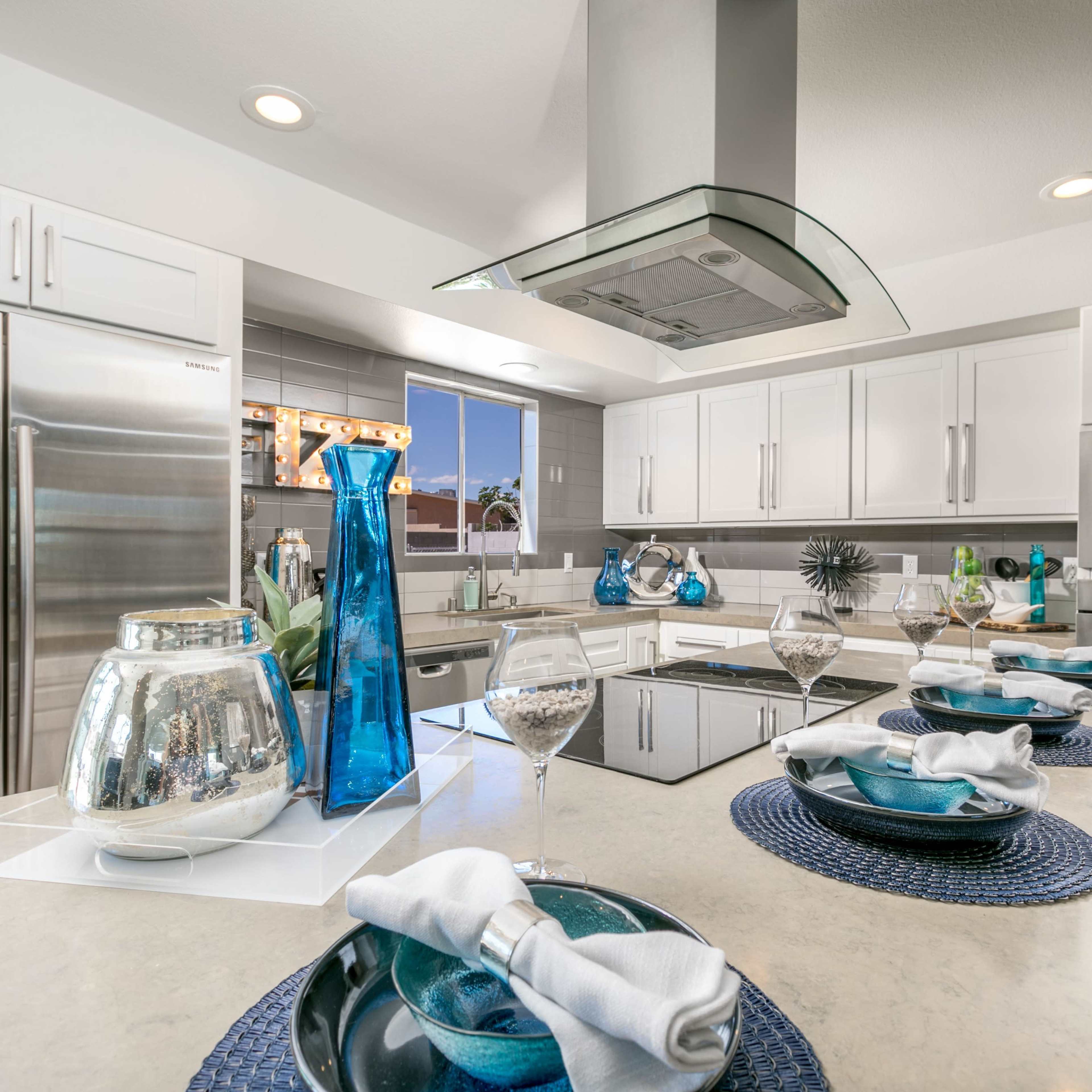 A modern kitchen with white cabinetry, stainless steel appliances, and a central island adorned with decorative glass vases and table settings.