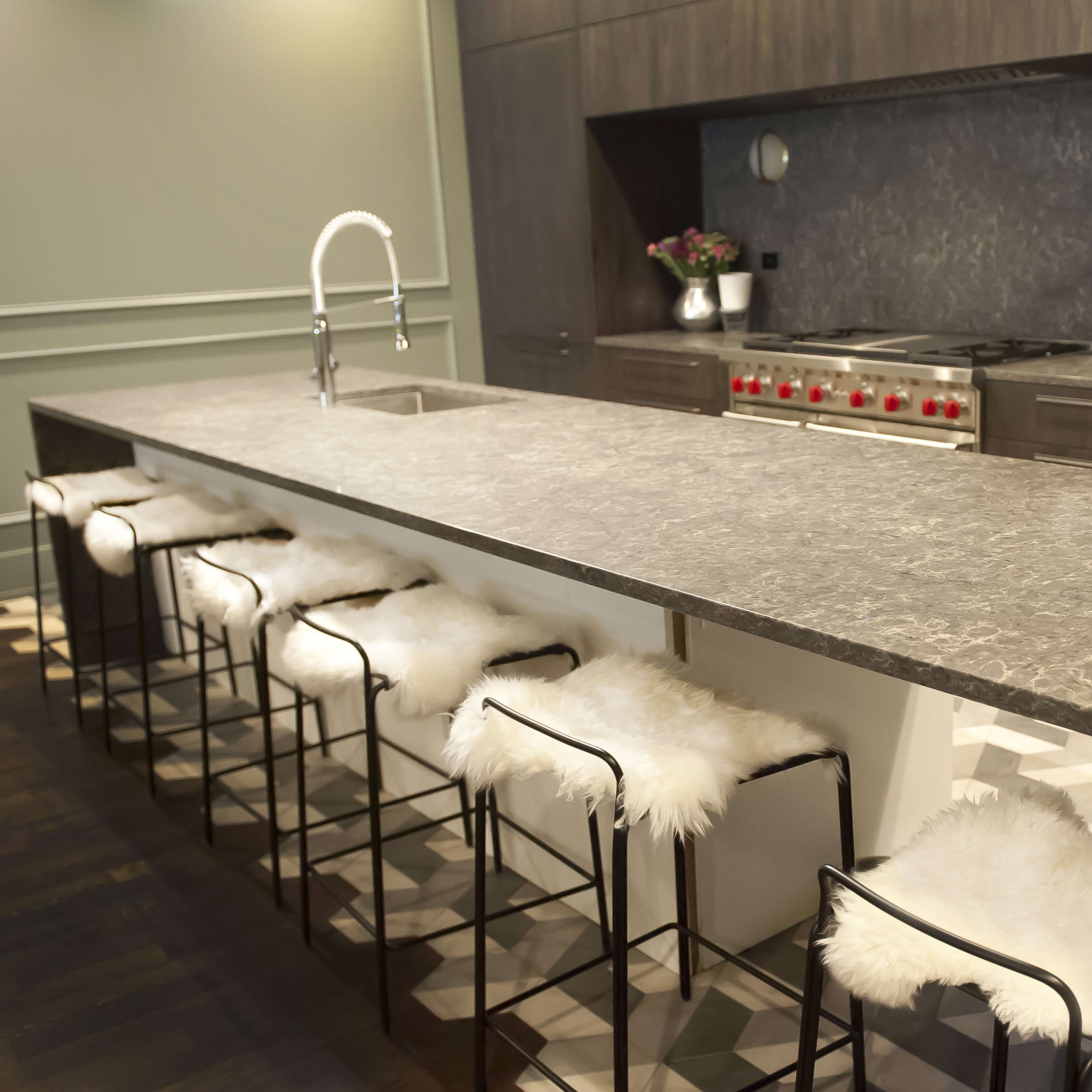 A modern kitchen features a large island with brown bar stools and a dark wood panel backsplash, complemented by stylish pendant lighting.