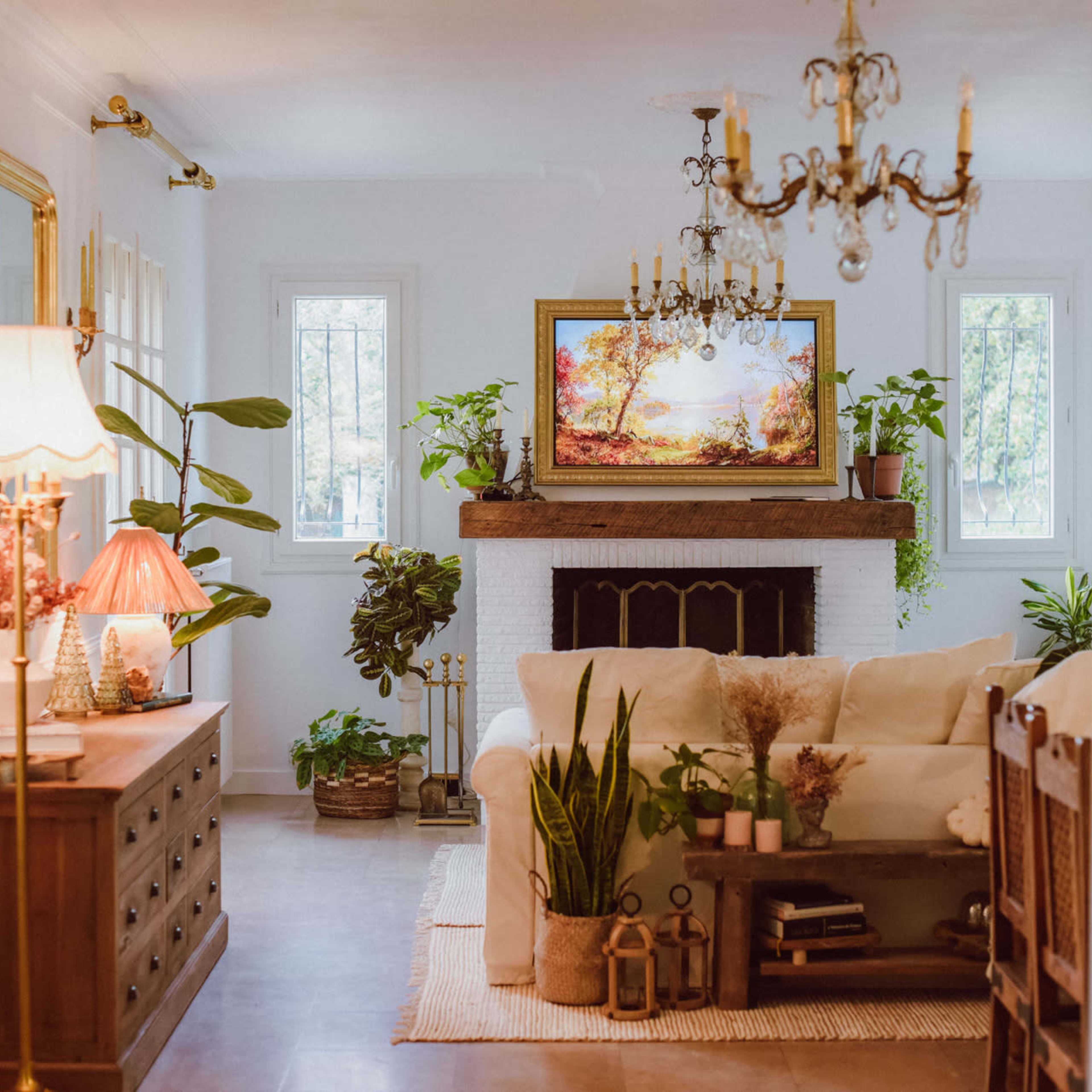 A living room with a white sofa, a wooden coffee table, a fireplace adorned with plants, and a chandelier hanging from the ceiling.