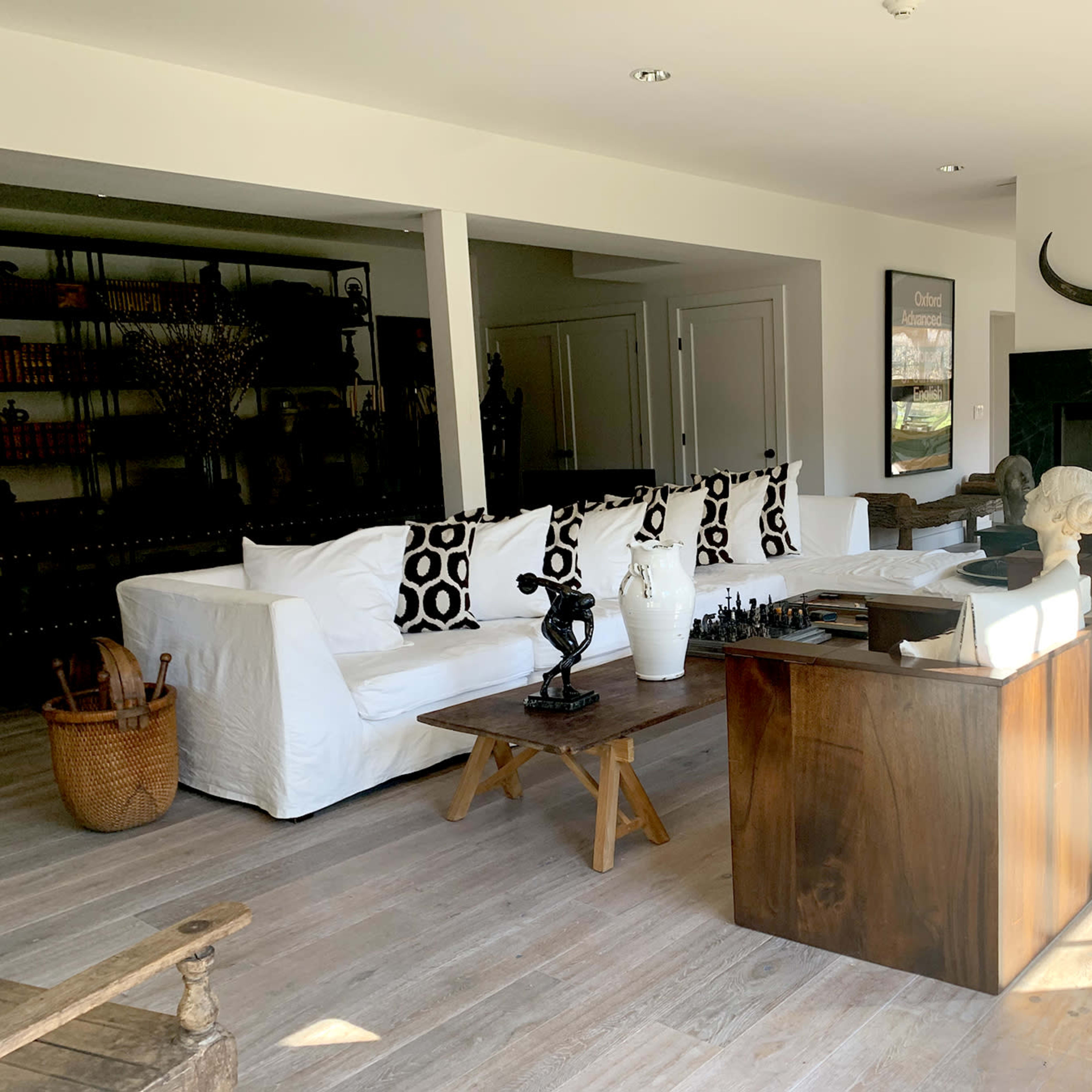 A modern living room with a white sofa, black and white patterned cushions, a wooden coffee table, and a fireplace, complemented by various decorative sculptures.