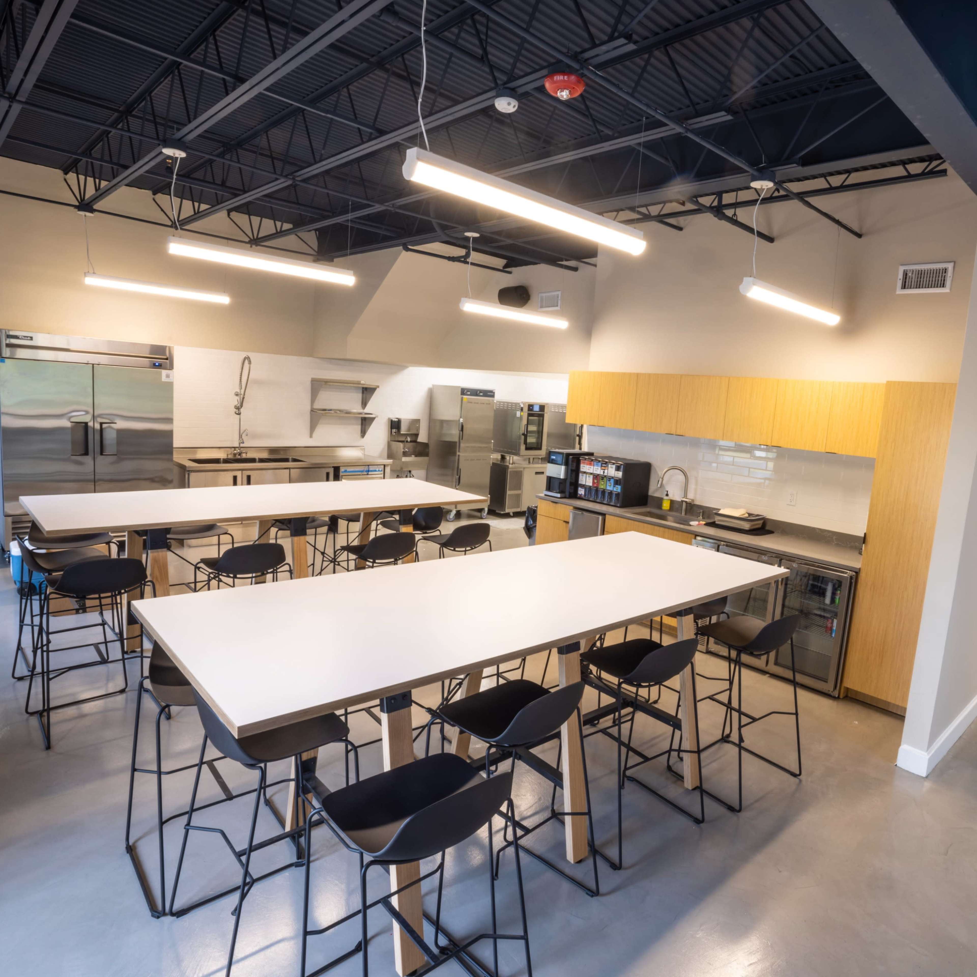 A modern kitchen and dining area with multiple high tables and black bar stools, large appliances, and a hallway leading to other rooms.