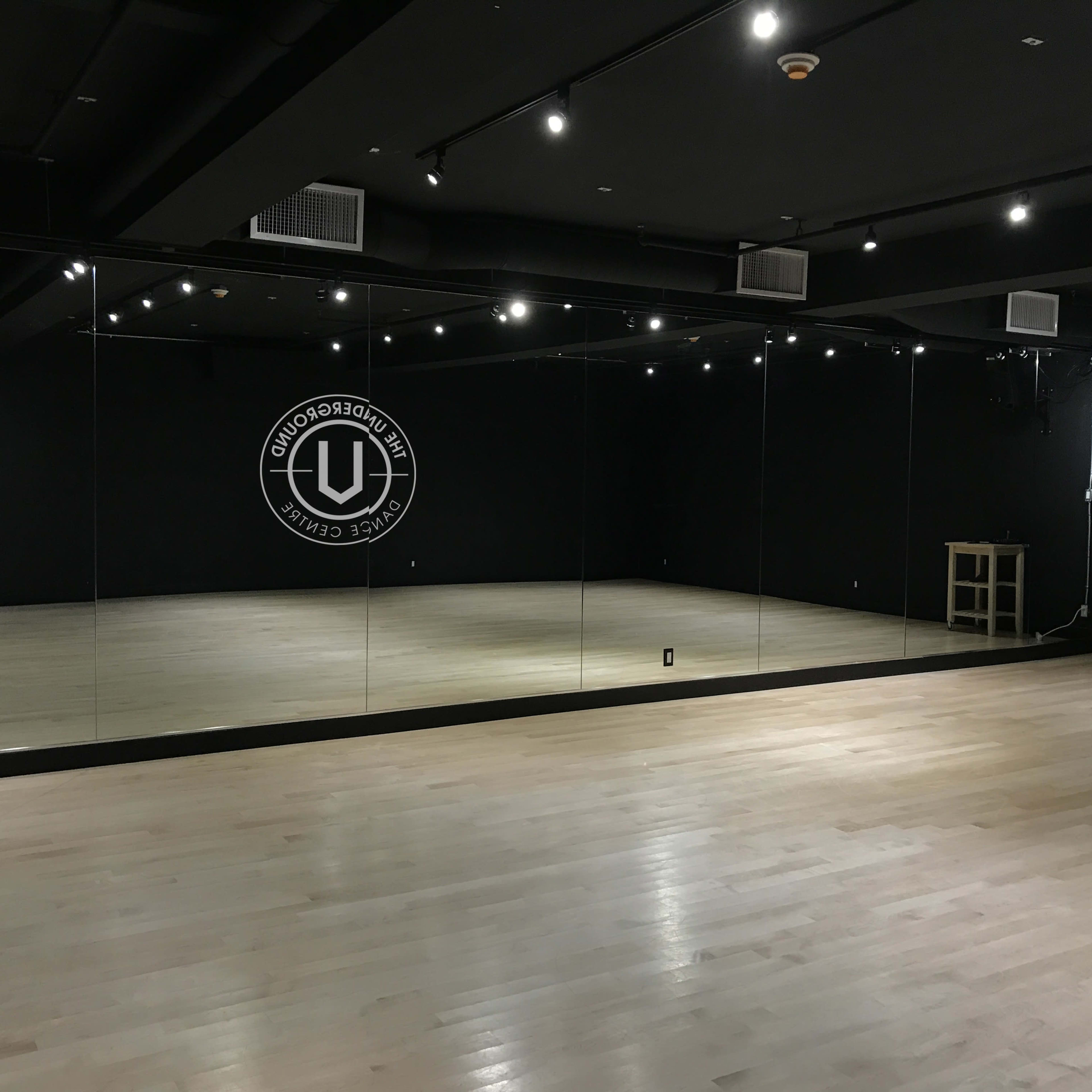 A spacious dance studio with mirrored walls and hardwood flooring, illuminated by overhead lights.